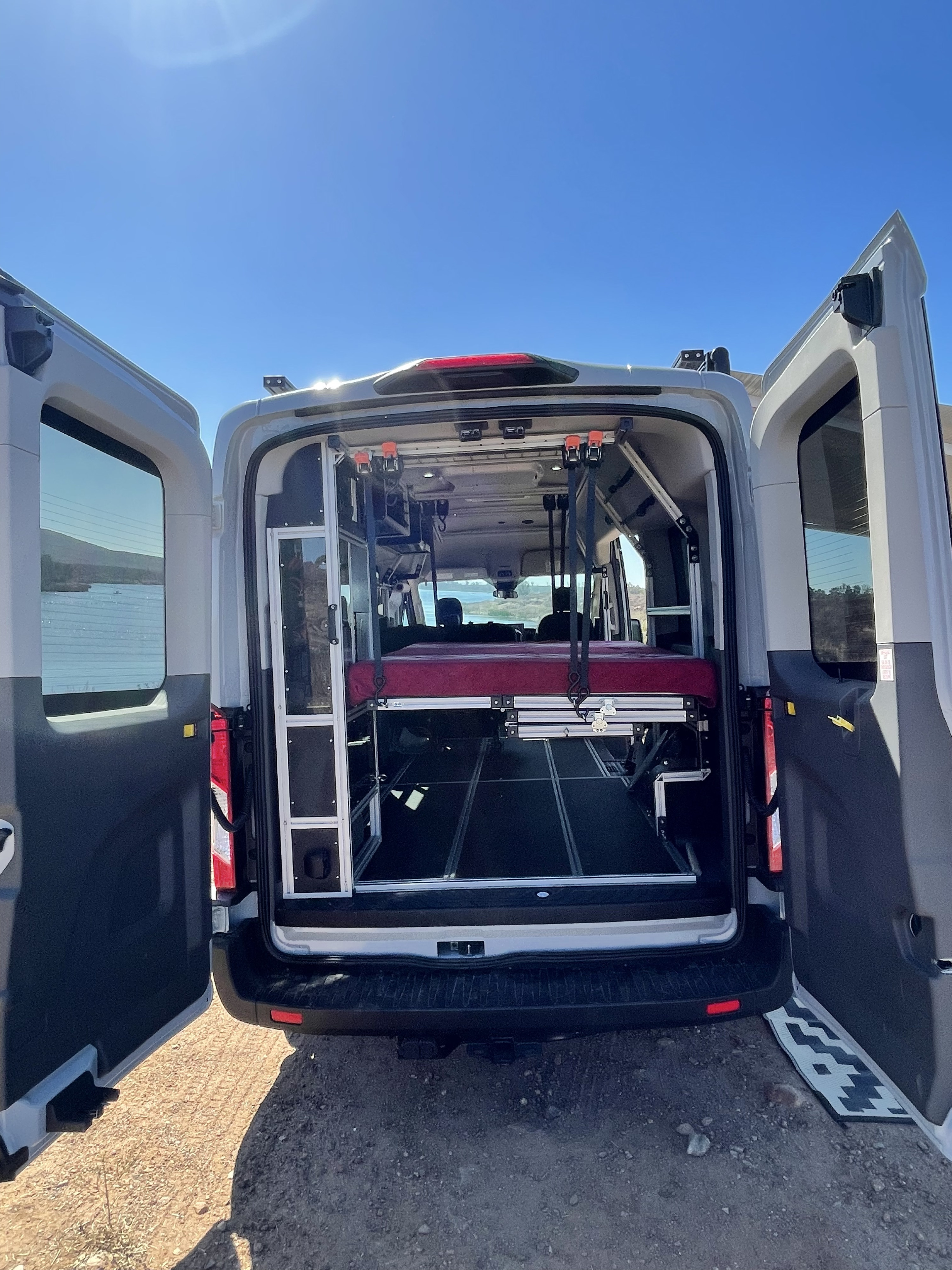 Discover the interior of this RV rental camper van with open rear doors, revealing a clever modular bed and storage system.. Ford Transit 2022