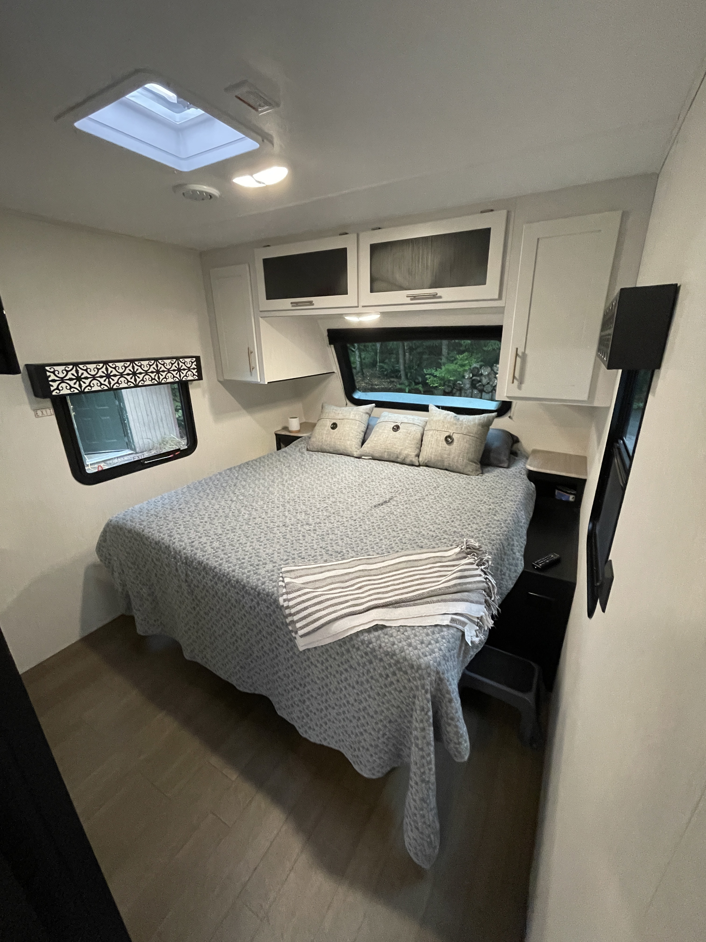 This RV rental bedroom features a comfy bed with grey bedding, overhead cabinets, and bright skylight, offering comfort for travelers.. Forest River Wildcat 266MEX 2022