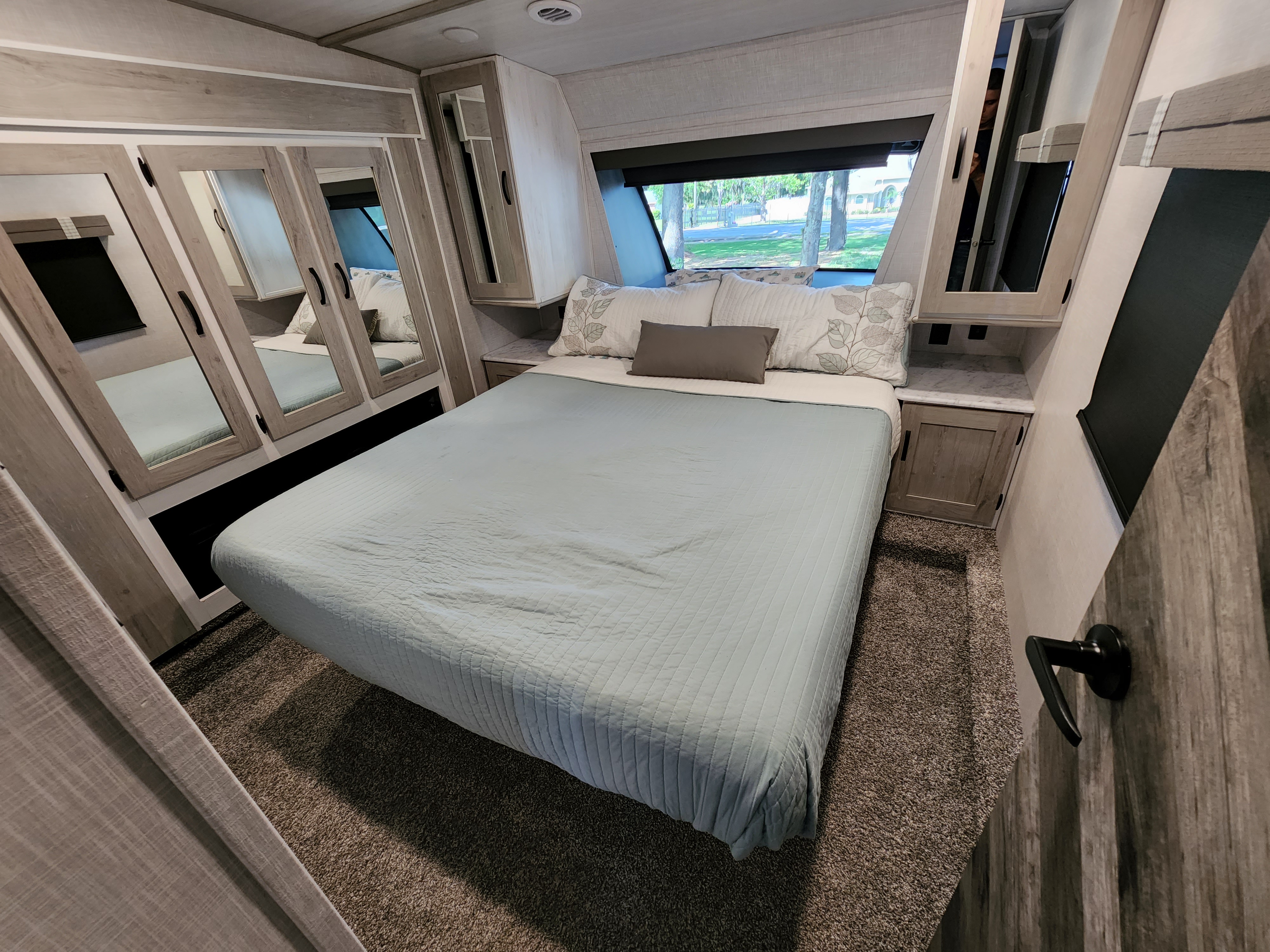 Spacious RV rental master bedroom with a comfortable bed, mirrored closets, and a large window.. Forest River Impression 2022