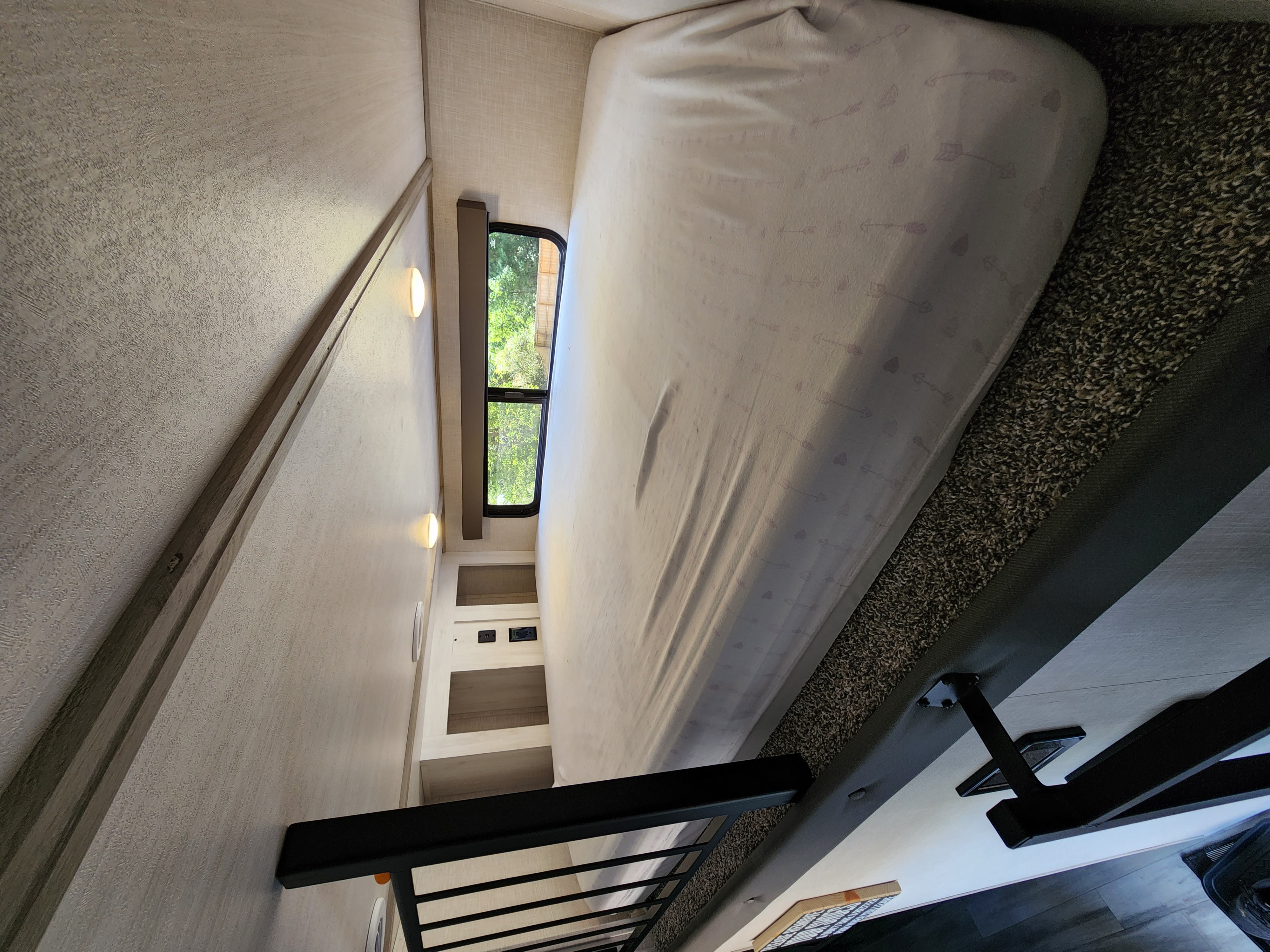 RV rental bedroom featuring a cozy bunk bed with arrow-patterned sheets, wall lighting, and a window overlooking greenery.. Forest River Impression 2022