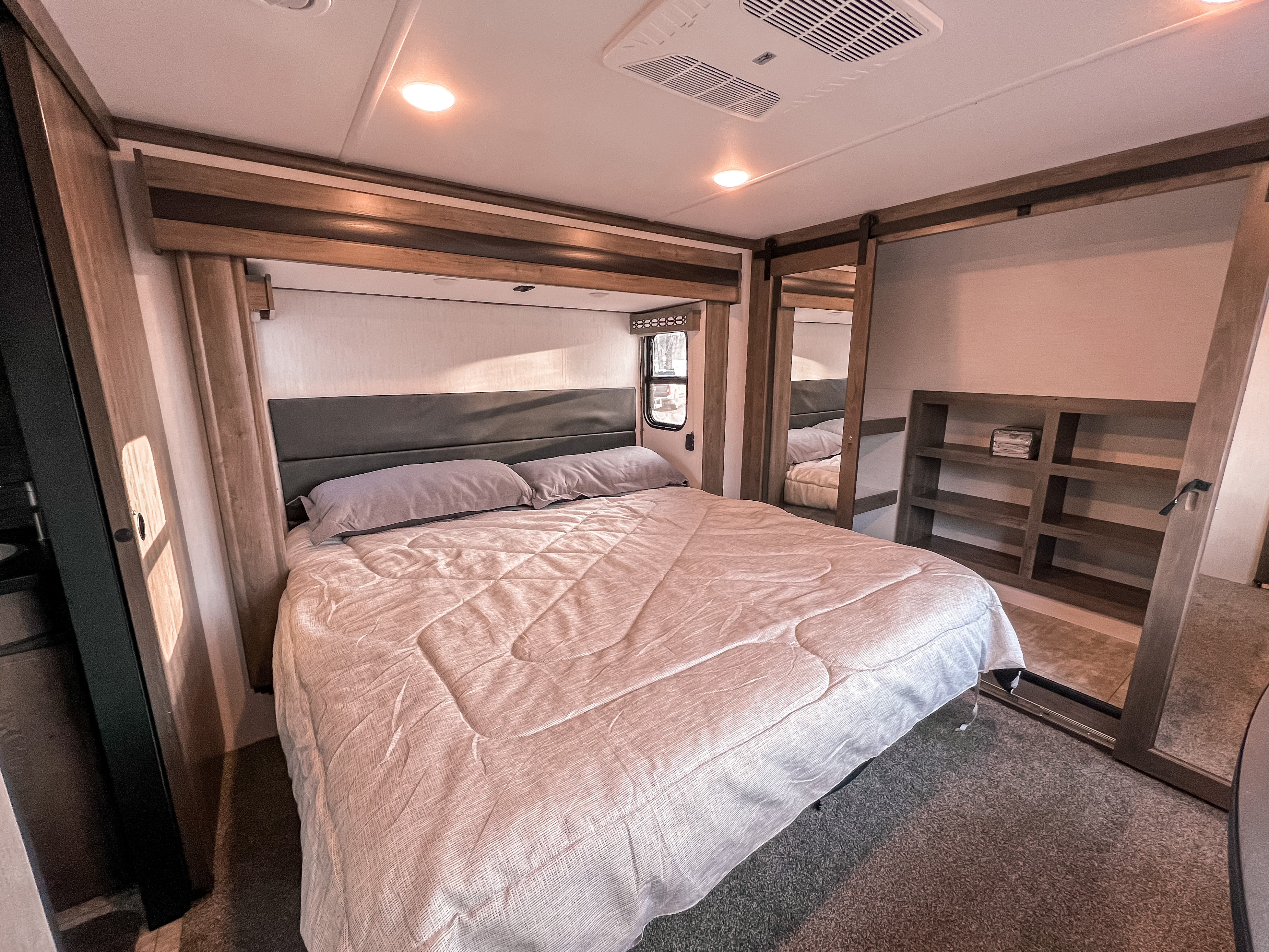 Discover comfort in this RV rental bedroom: a cozy bed, mirrored closet, and shelving unit offer practical space for your travels.. Forest River Vengeance 2023