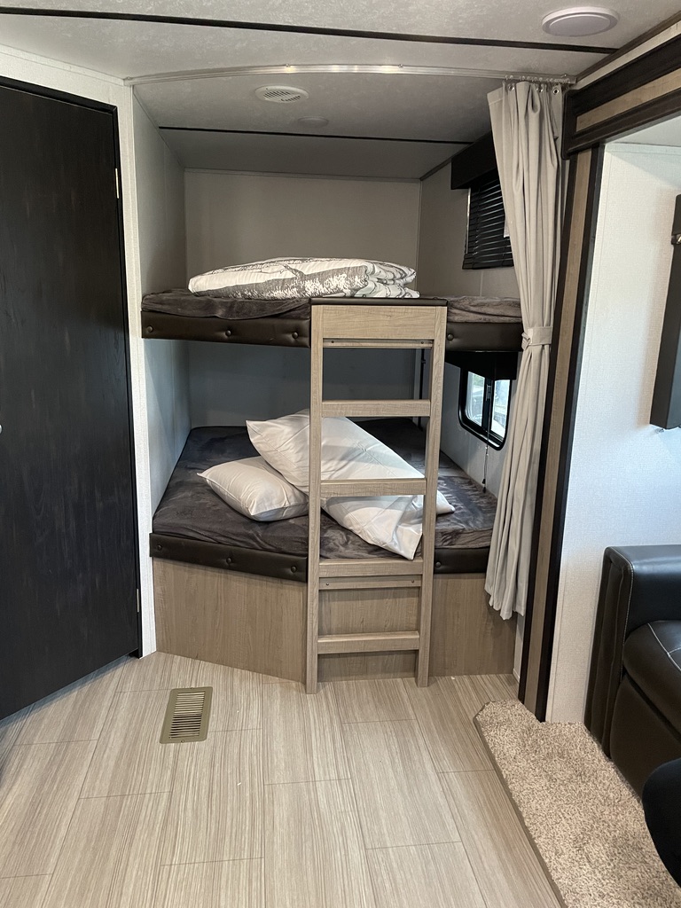 RV rental bunk beds: A cozy sleeping area with ladder, bedding, and wood-look flooring, perfect for family adventures.. Keystone RV Hideout 2020