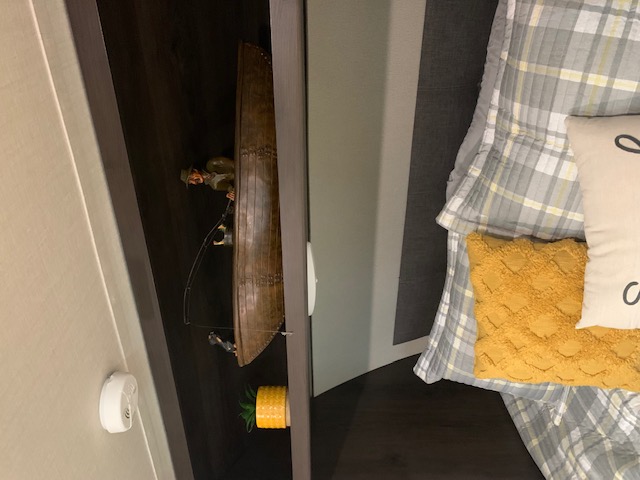 RV rental bed area with cozy plaid bedding, yellow throw pillow, and a unique shelf displaying a fishing boat figurine.. Grand Design Transcend Xplor 2022