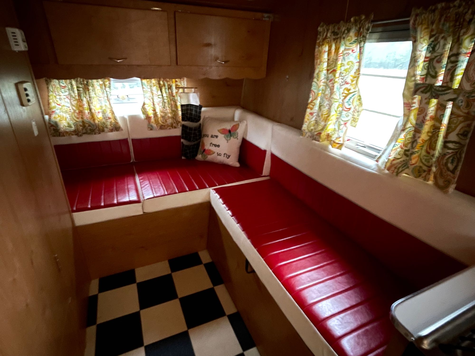 Step inside this cozy RV rental's dinette, featuring vibrant red seating, a checkered floor, and colorful curtains.. Forest River Shasta Airflyte 2015