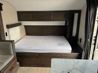 Cozy RV rental interior: A dark wood bedroom with a large bed, white bedding, overhead cabinets, and a side dinette seat.. Forest River Grey Wolf 27RR 2020