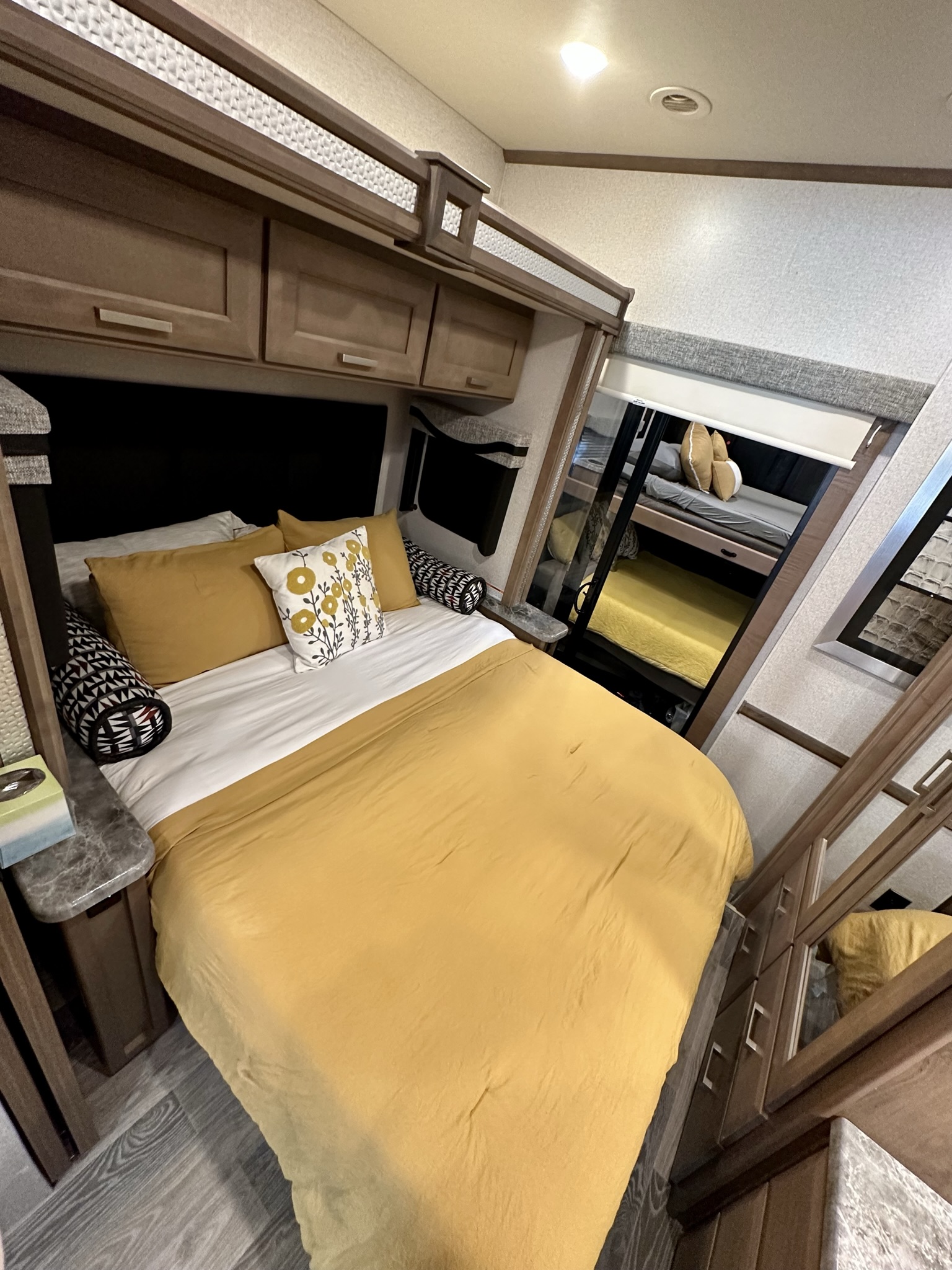 Explore this RV rental bedroom featuring a yellow bed, overhead cabinets, and a reflective view of bunk beds.. Thor Motor Coach Outlaw 2023