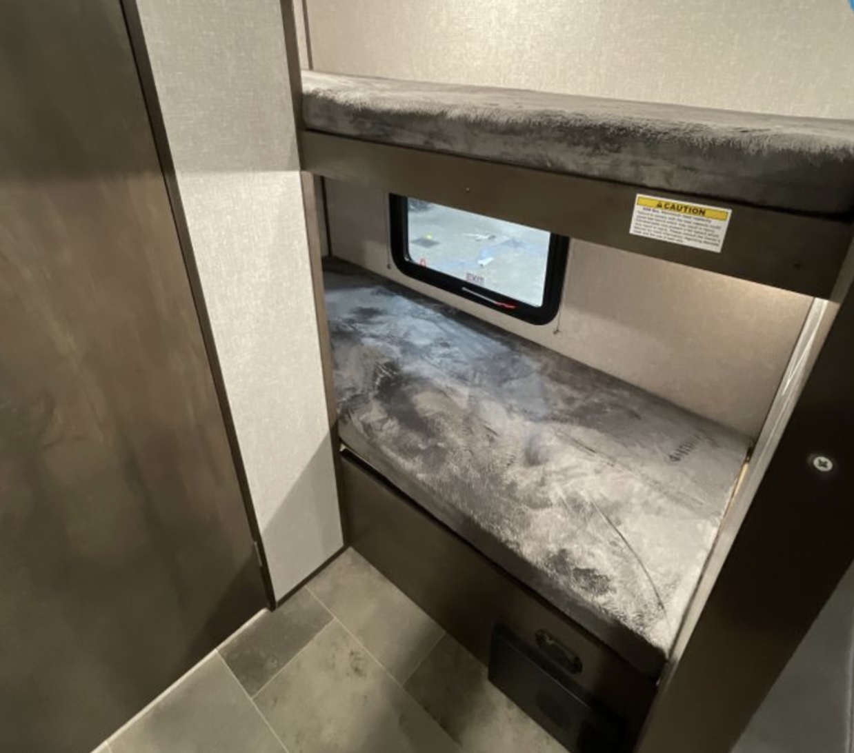 Comfortable bunk beds with soft mattresses and a window in this RV rental provide cozy sleeping space.. Coleman Lantern 17B 2023