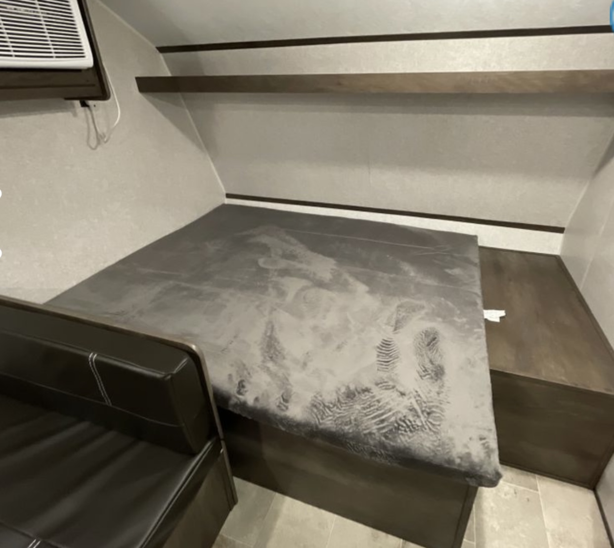 Inside an RV rental: compact sleeping area with visible footprints, a dinette seat, & overhead shelves.. Coleman Lantern 17B 2023