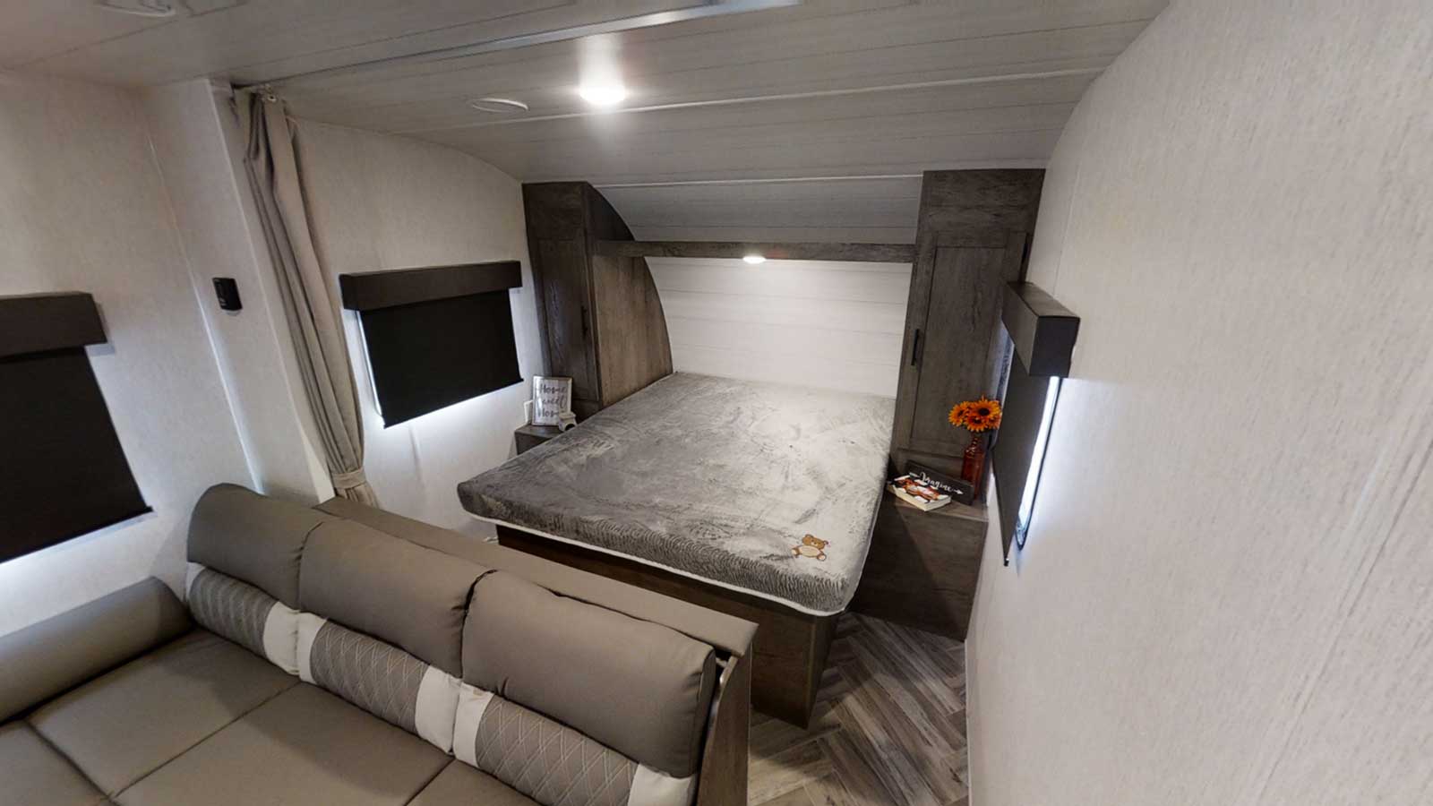 RV rental interior showcasing a comfortable bed, sofa area, and built-in storage. Modern and bright.. Forest River Wildwood X-Lite 2023