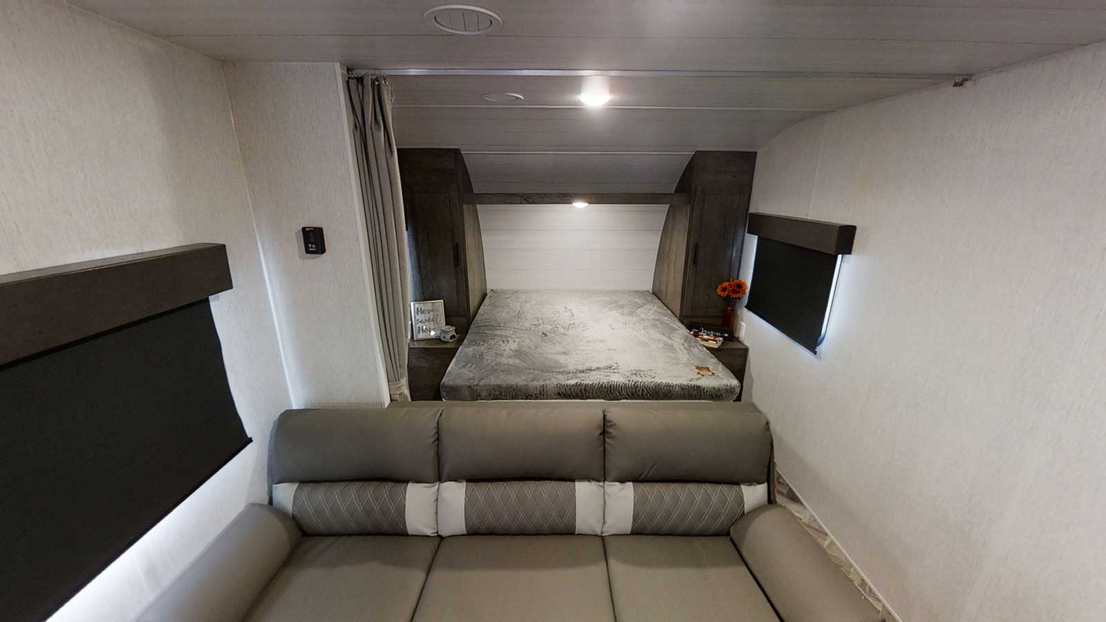 Clean, modern RV rental interior with a cozy bedroom (bed, cabinets) and comfy sofa. Compact living for your journey.. Forest River Wildwood X-Lite 2023