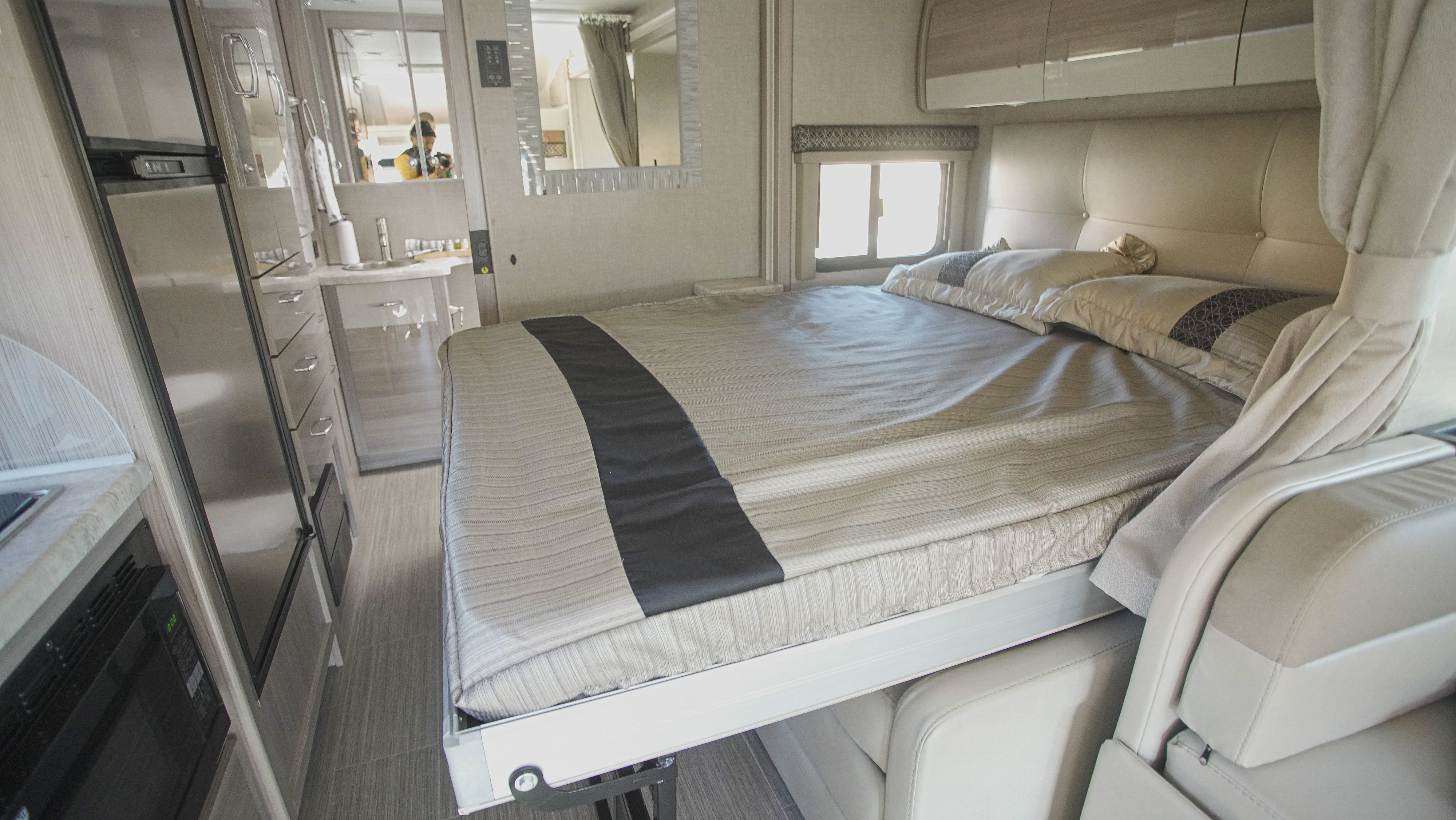Comfortable RV rental interior showing a raised bed over lounge seating, with a compact kitchen & bathroom vanity.. Thor Motor Coach Tiburon 24FB 2023