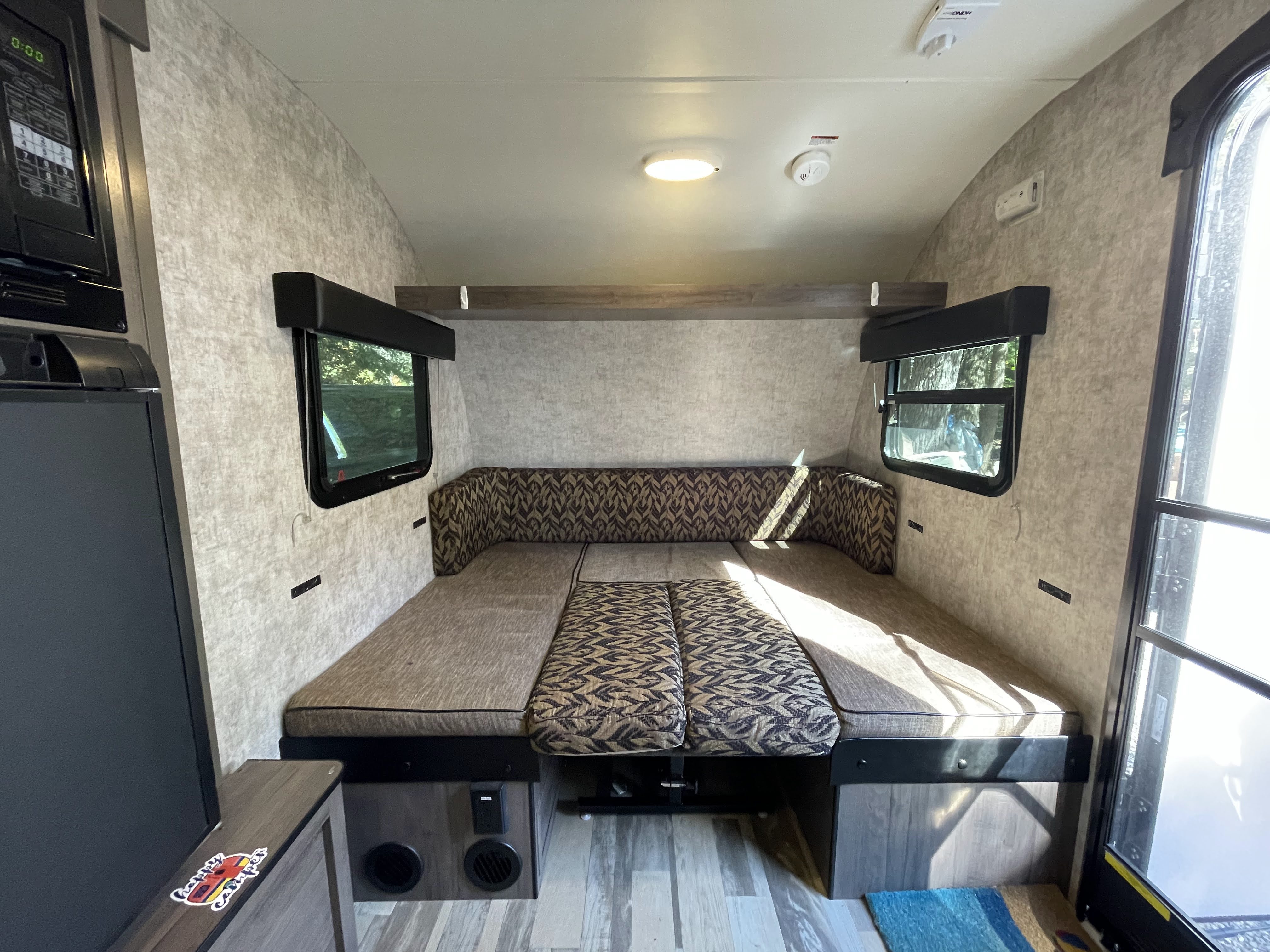 Cozy rv rental interior featuring a dinette with patterned cushions that converts to a bed, visible windows, and a microwave.. Winnebago Winnie Drop 170k 2017
