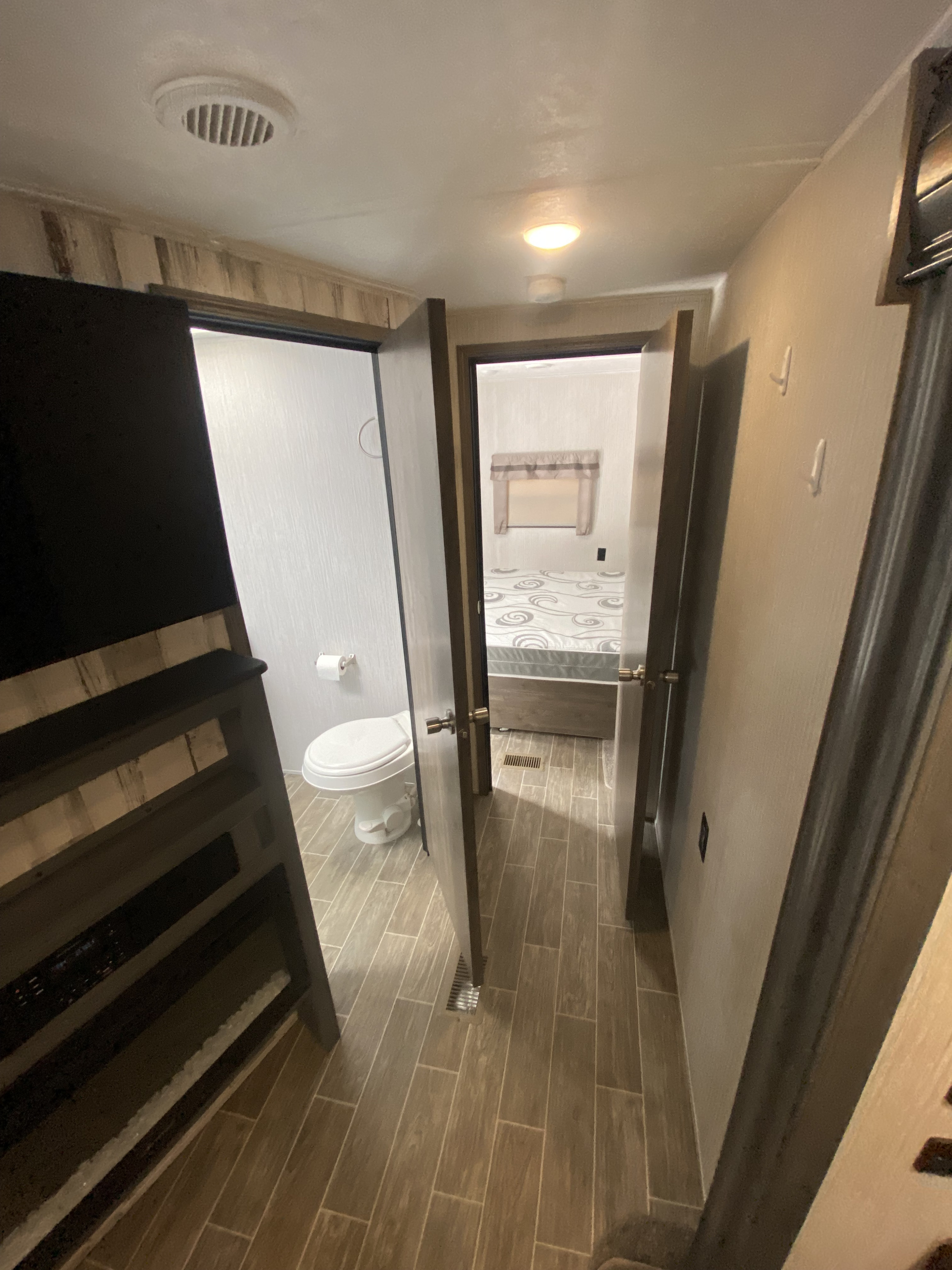 Explore an RV rental interior: a compact hallway with an open bathroom (toilet) and a bedroom. Bunk beds are to the left.. Forest River Palomino Puma 2020