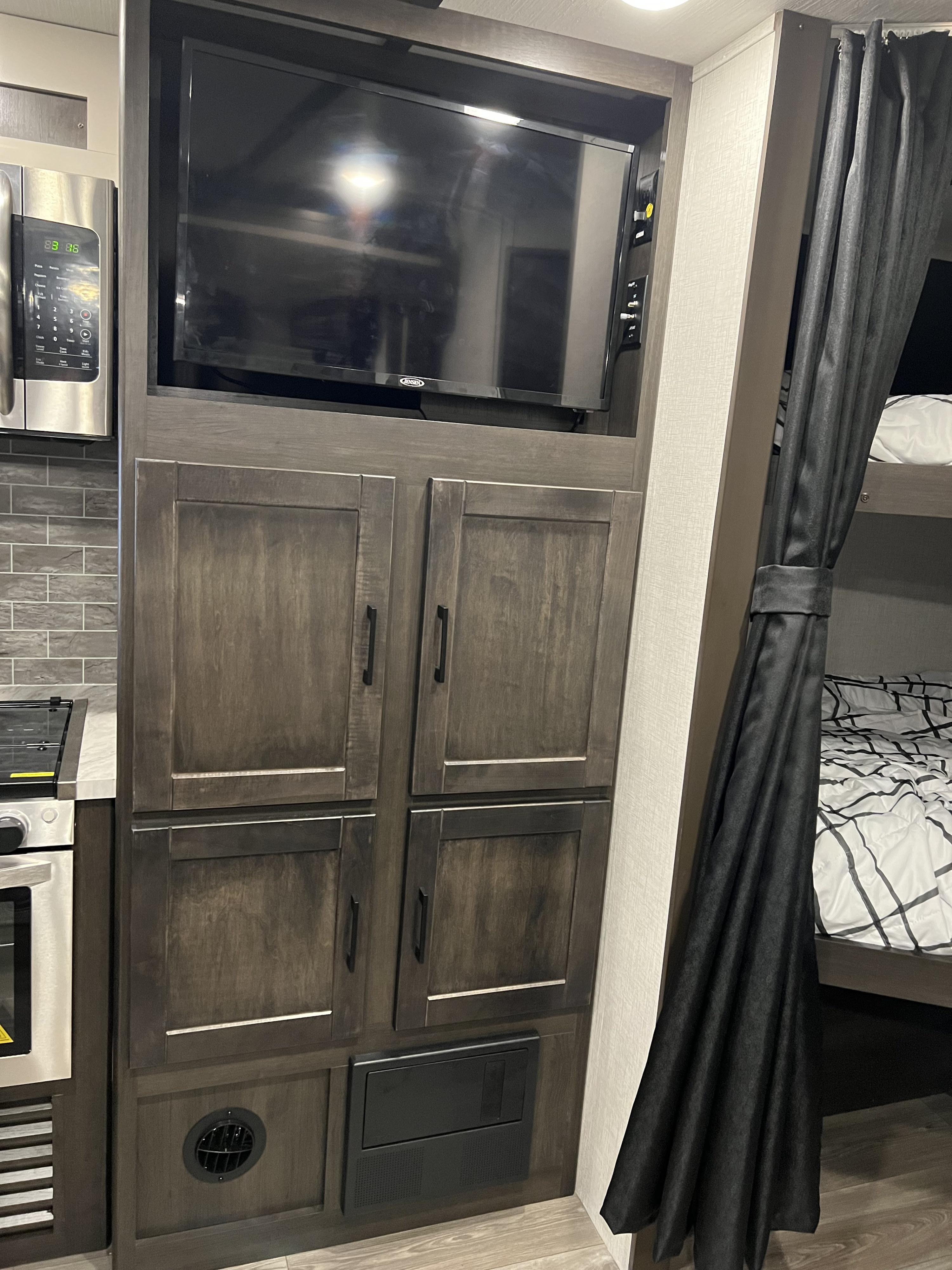 Cozy RV rental interior: kitchen with microwave, TV, ample storage, and bunk beds with a privacy curtain.. Crossroads RV Cruiser Aire 2022