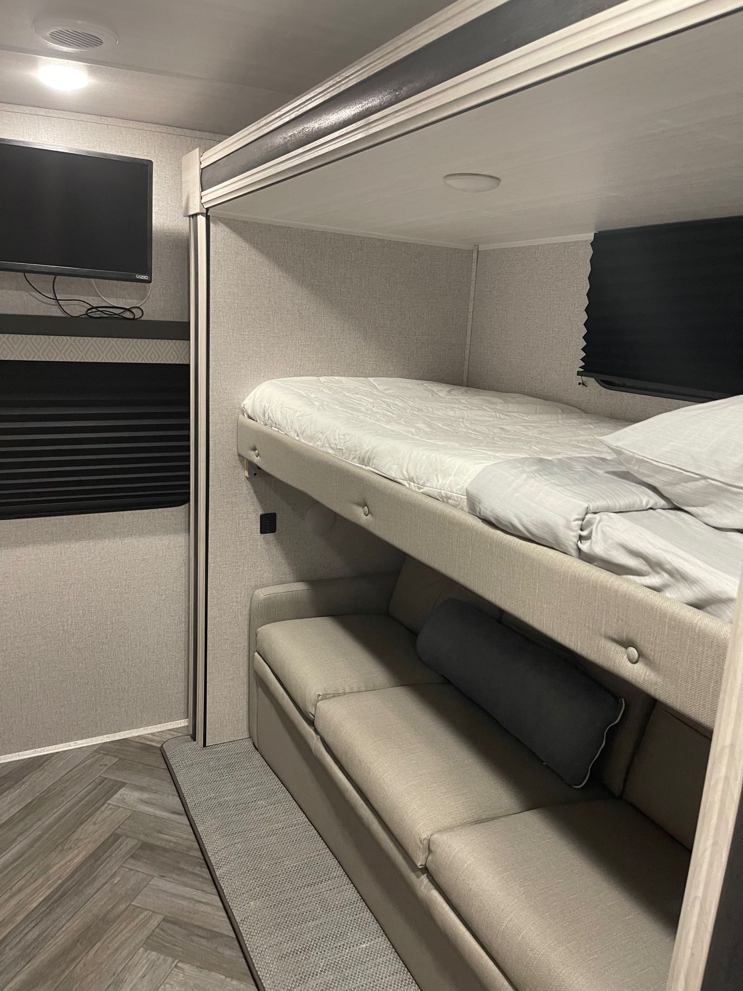 RV rental bunkhouse: Camper interior with an upper bunk bed, lower sofa, wall TV, and herringbone-patterned floor.. Della Terra 312H Della Terra 2023