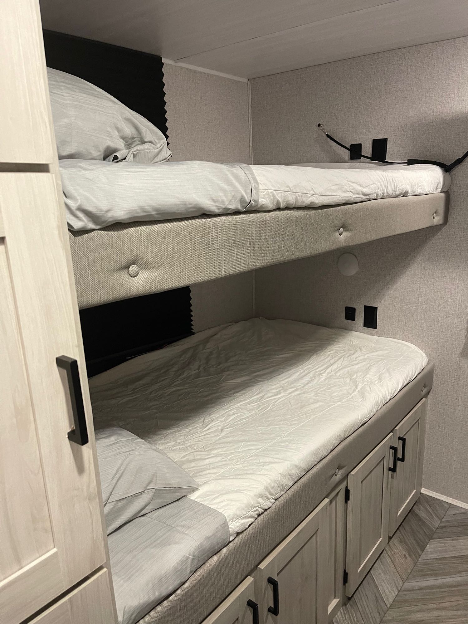Cozy bunk beds in an RV rental, featuring light grey bedding, storage cabinets, and power outlets for a comfortable stay.. Della Terra 312H Della Terra 2023