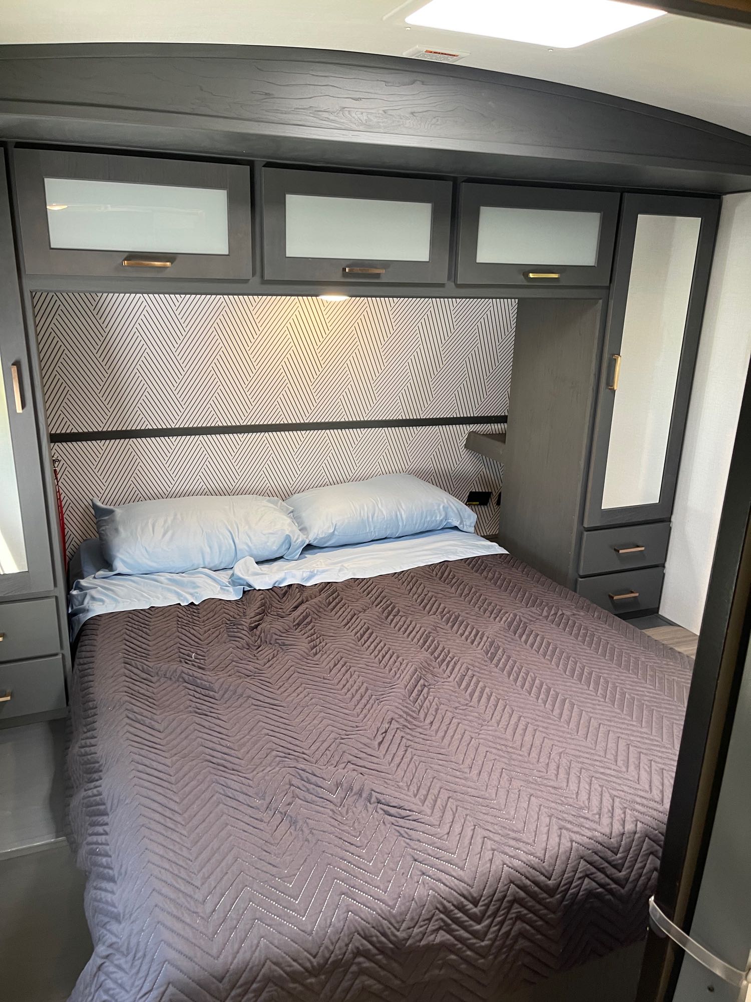 Cozy RV rental bedroom featuring a comfy bed, stylish patterned headboard, and functional overhead cabinets.. Keystone Bullet 250BHS 2022