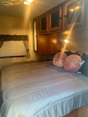 Cozy RV rental bedroom featuring a comfortable bed with soft pillows, wooden cabinets, and a window for natural light.. Heartland RVs North Trail 2012