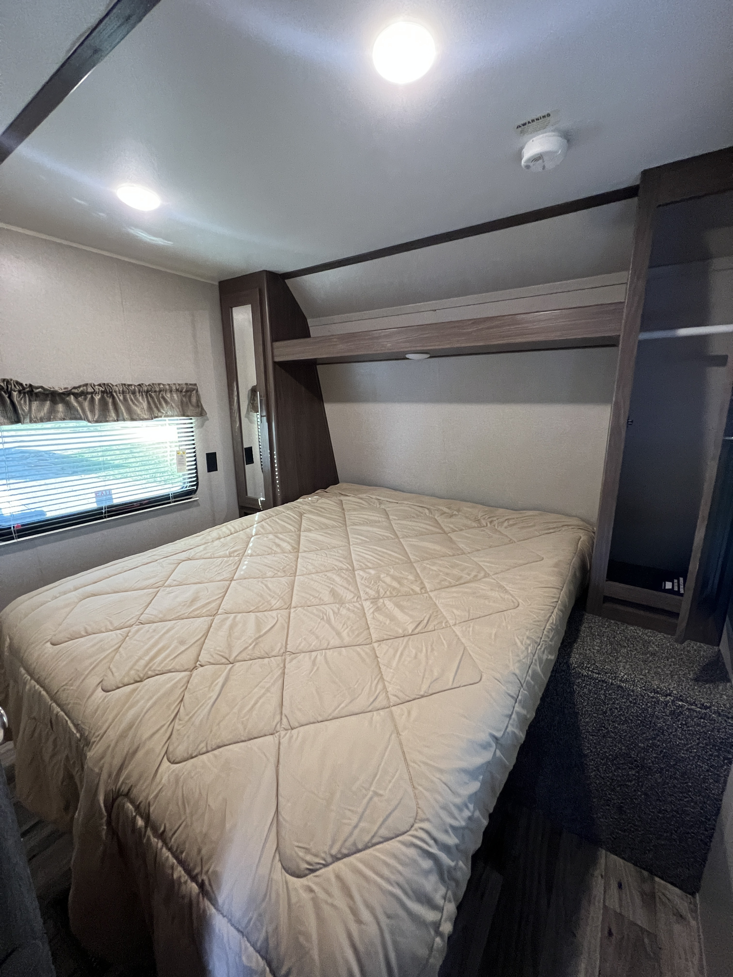 Cozy RV rental bedroom features a queen bed with a light brown comforter, a window, built-in storage, and ceiling lights.. Keystone RV Hideout LHS 2020