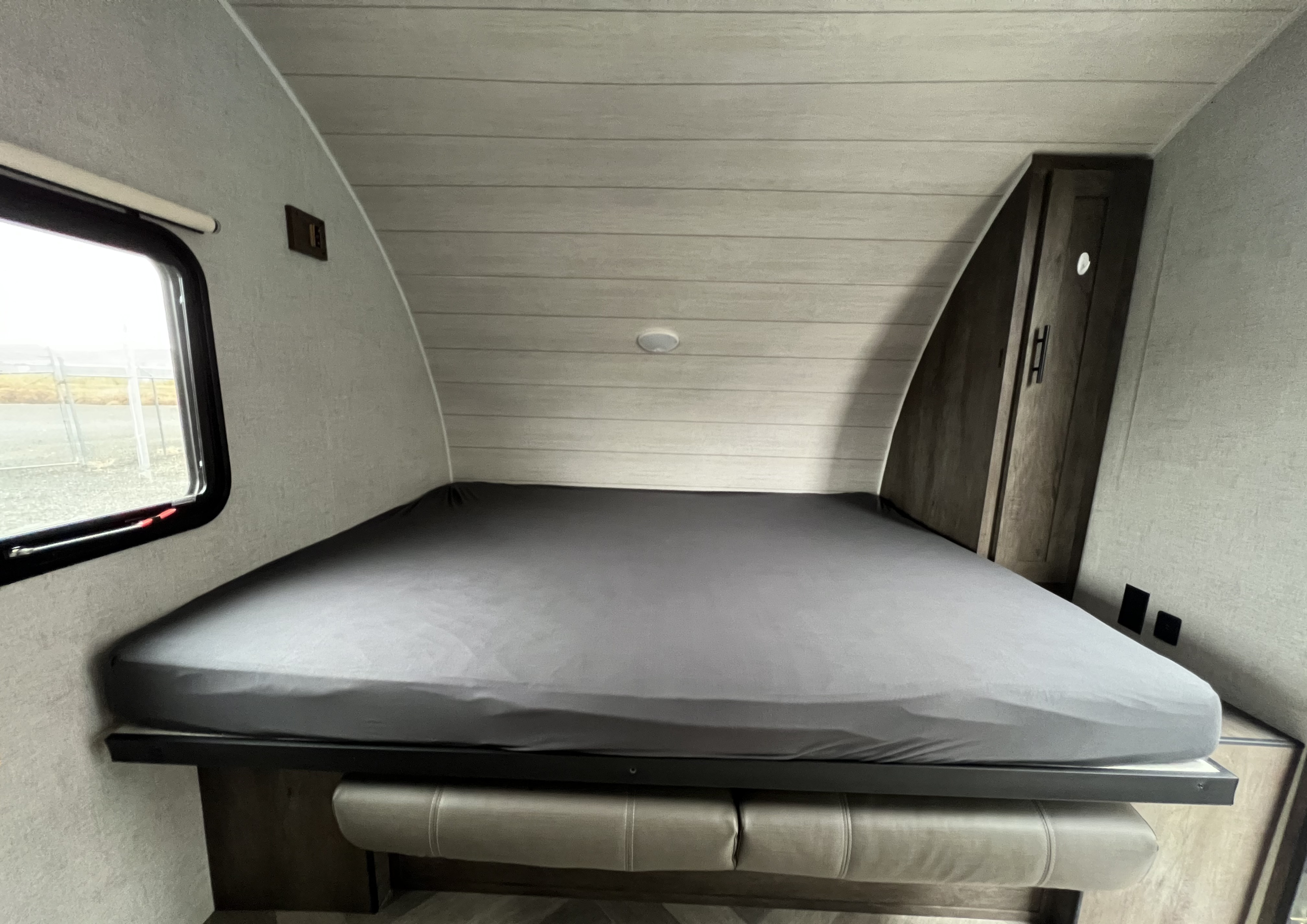 Inside a cozy RV rental: a comfortable bed with grey sheet, window, and integrated storage. Perfect for road trips!. Forest River Salem 2020