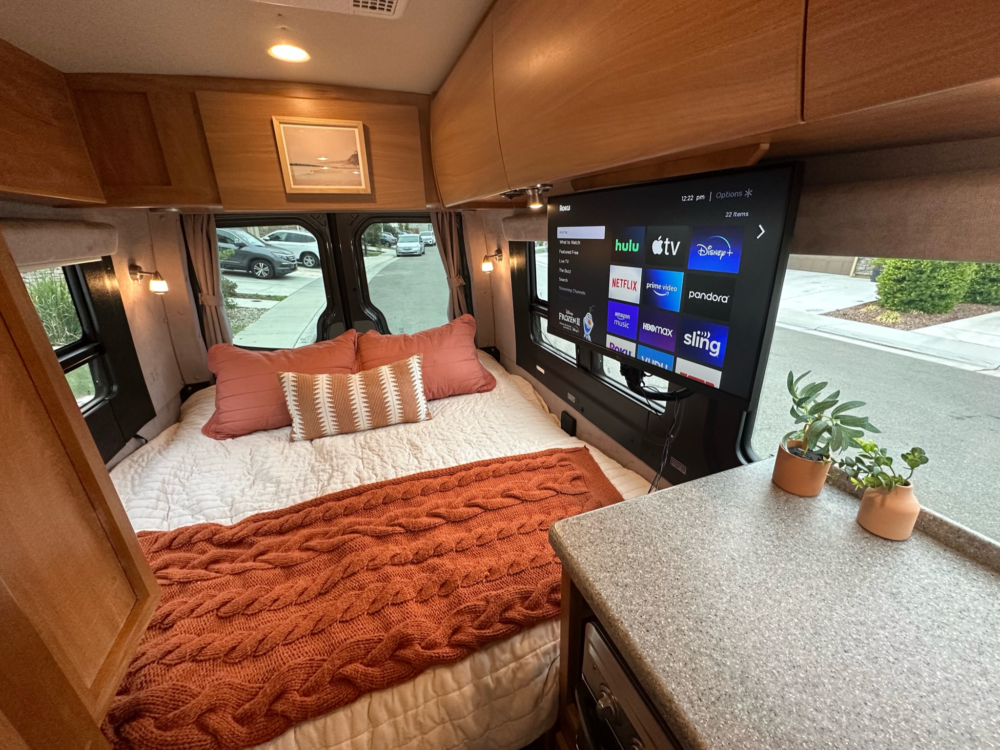 Cozy RV rental interior with a large bed, TV showing streaming apps, and wooden cabinets. Ideal for comfortable travel.. ERA Era 2010