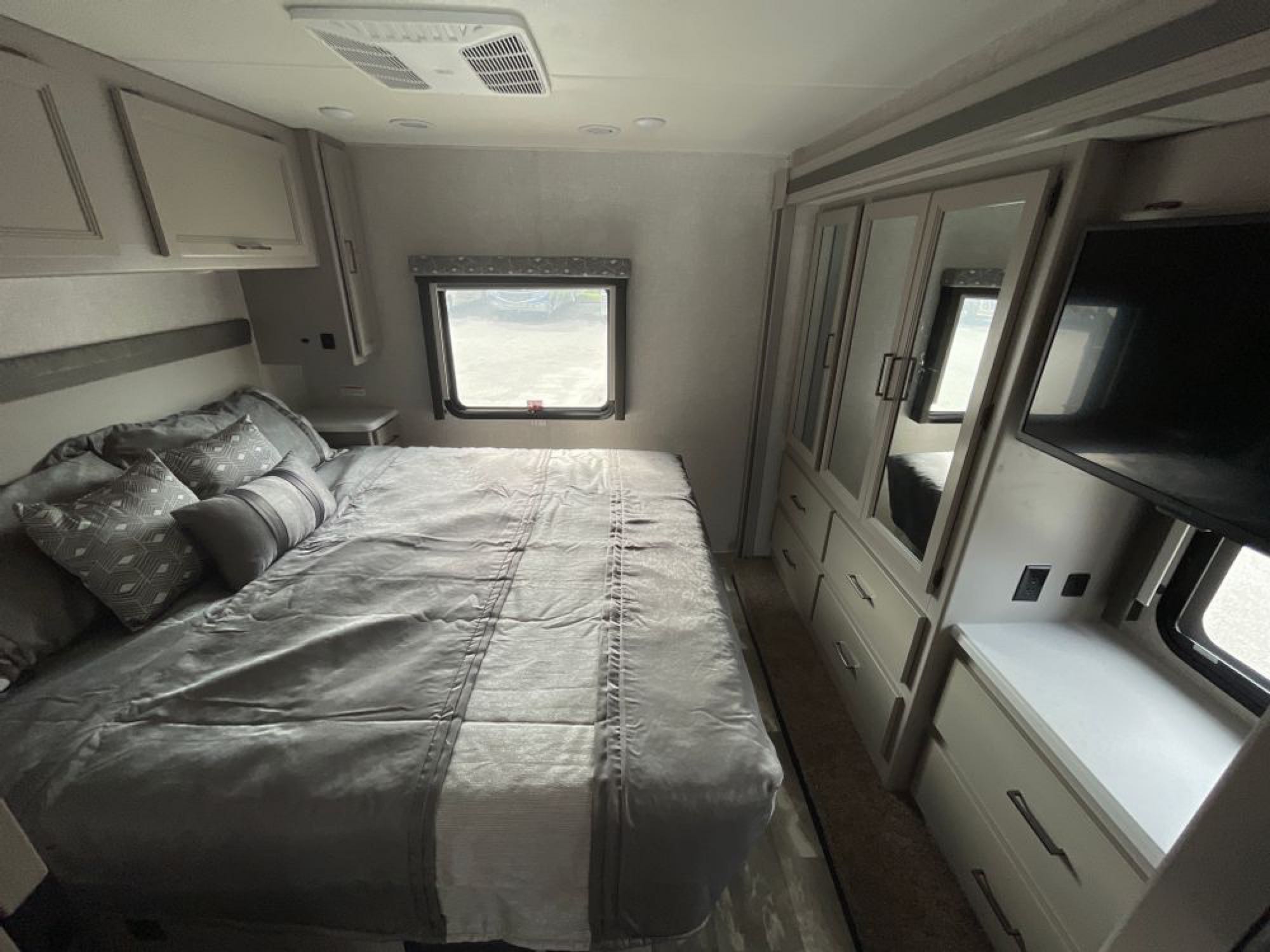 RV rental bedroom with queen bed, overhead cabinets, wardrobe, TV, and window. Cozy, modern interior design.. Ford Windsport 2023