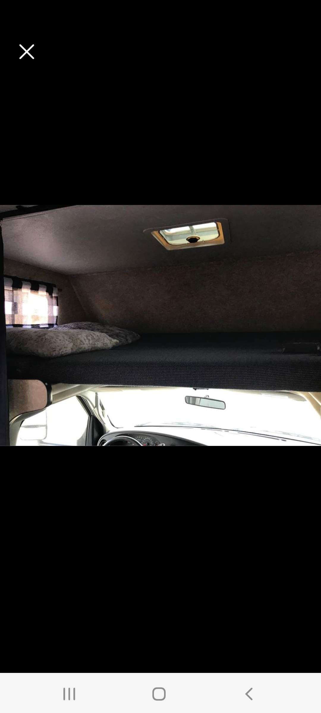 RV rental interior: comfy cab-over bunk with pillows, window, and overhead vent. Driver's dash visible below.. Thor Majestic 2009