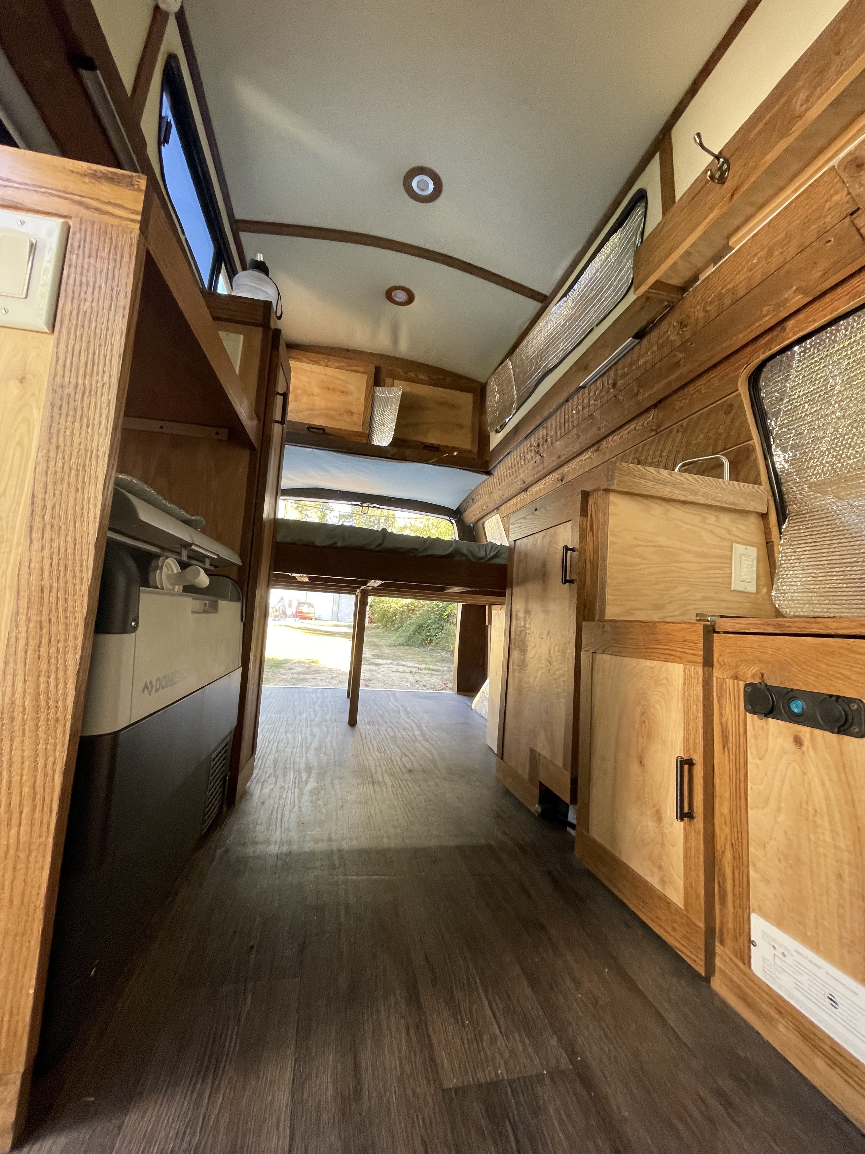 Spacious custom RV rental interior with wood cabinets, comfy bed, Dometic fridge, and wood floors. Ideal for road trips.. Chevrolet Express EXT 3500 2008