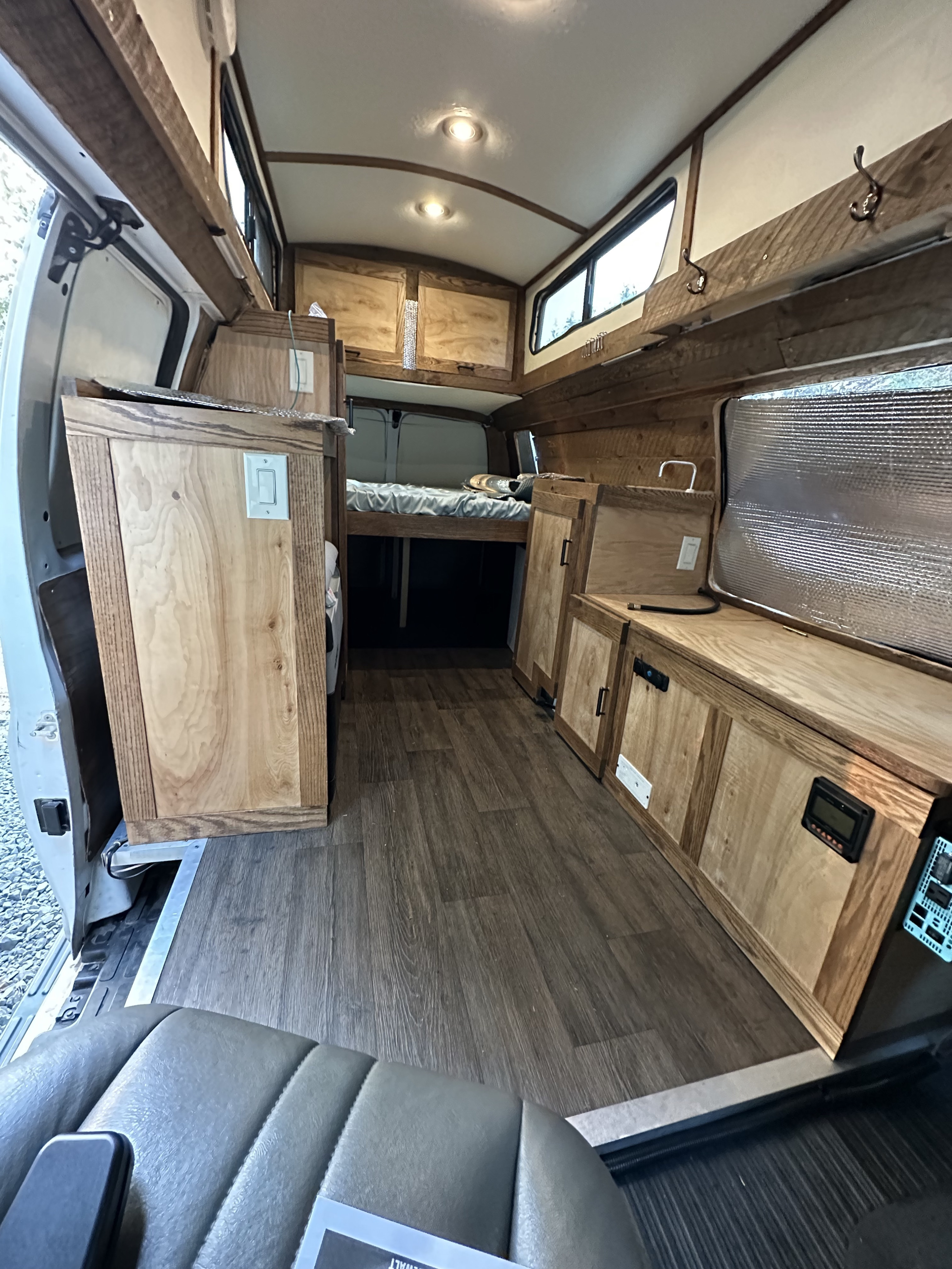 Inside a unique RV rental: custom wood interior, bed, kitchen counter, and wood-look flooring for cozy travel.. Chevrolet Express EXT 3500 2008