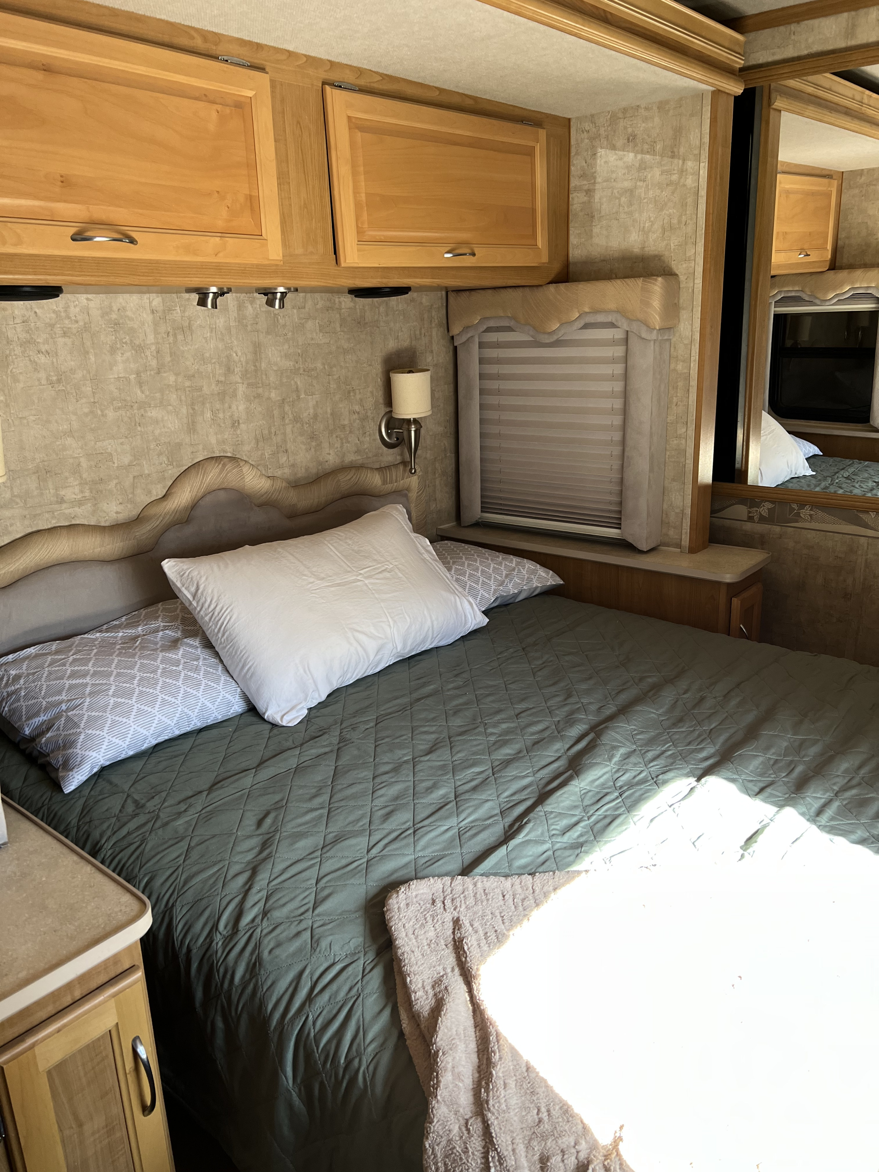 RV rental bedroom featuring a bed with quilted comforter, overhead cabinets, and window. Ideal for road trips.. Ford Bounder 2008