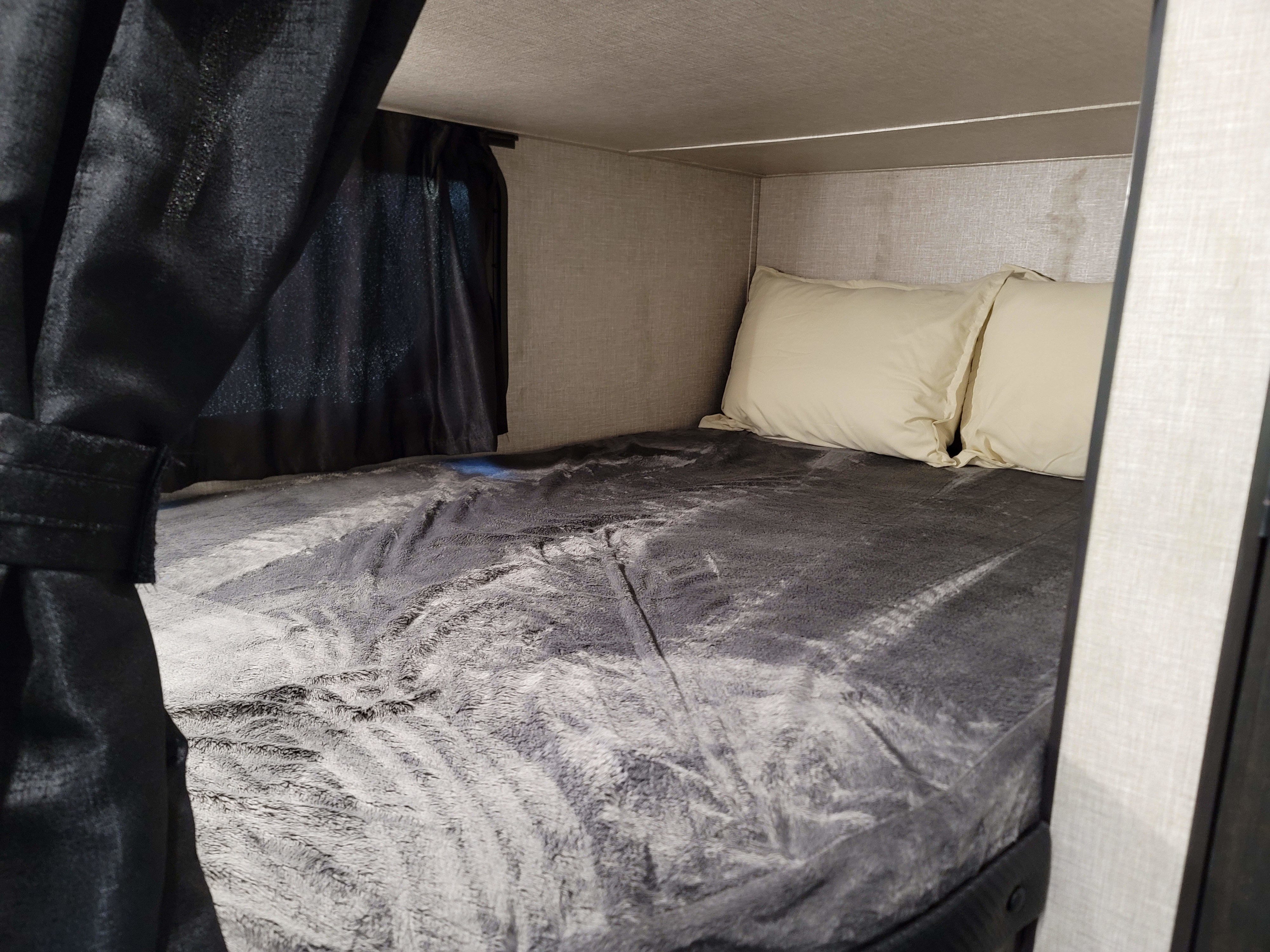 Cozy RV rental bed with dark curtains, a soft gray blanket, and light pillows, ideal for comfortable camper sleeping.. Jayco Jay Flight SLX 2022