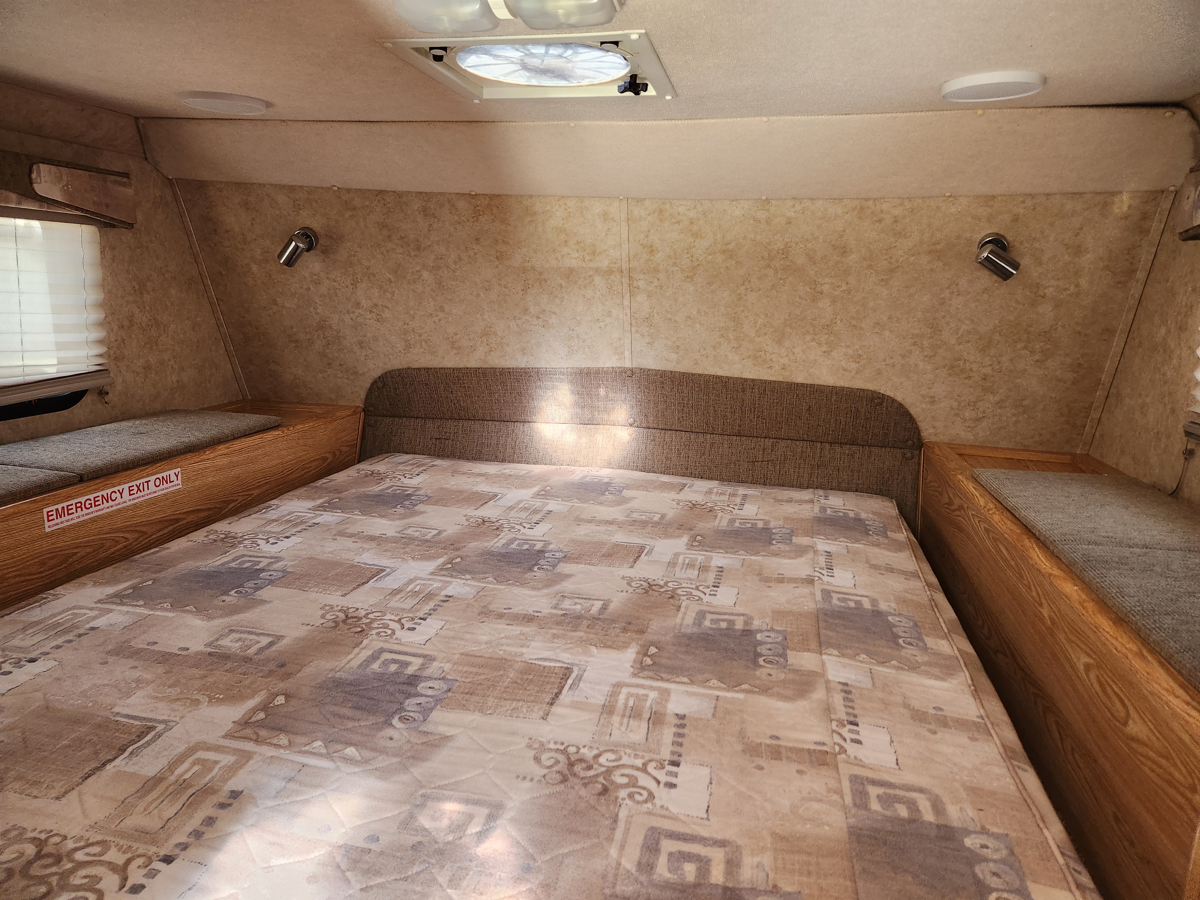 Cozy RV rental sleeping area featuring a patterned bed, built-in side benches, ceiling fan, and emergency exit.. Dodge Dodge Bighorn 3500 Heavy Duty Pu 2007