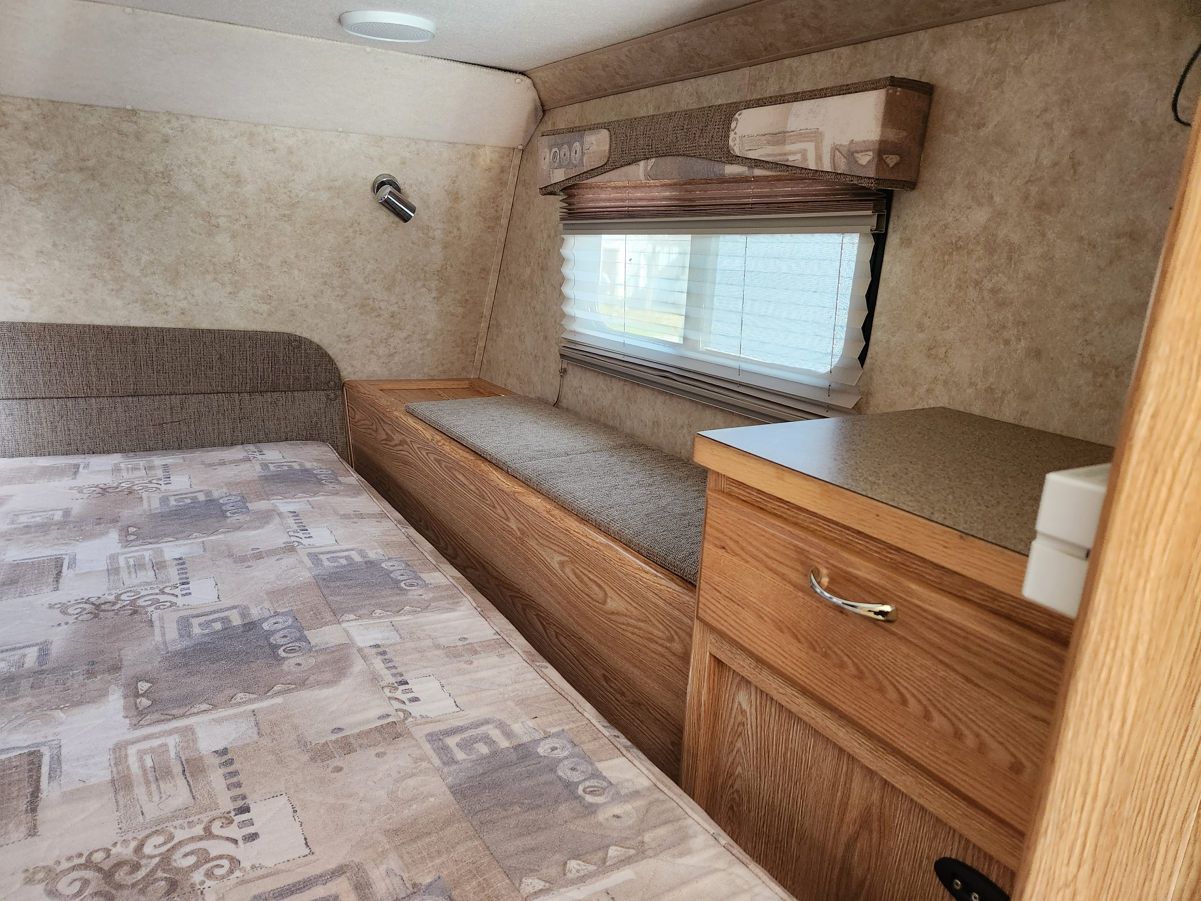 An RV rental's bedroom area: patterned bed, wooden built-in storage, and window with blinds.. Dodge Dodge Bighorn 3500 Heavy Duty Pu 2007