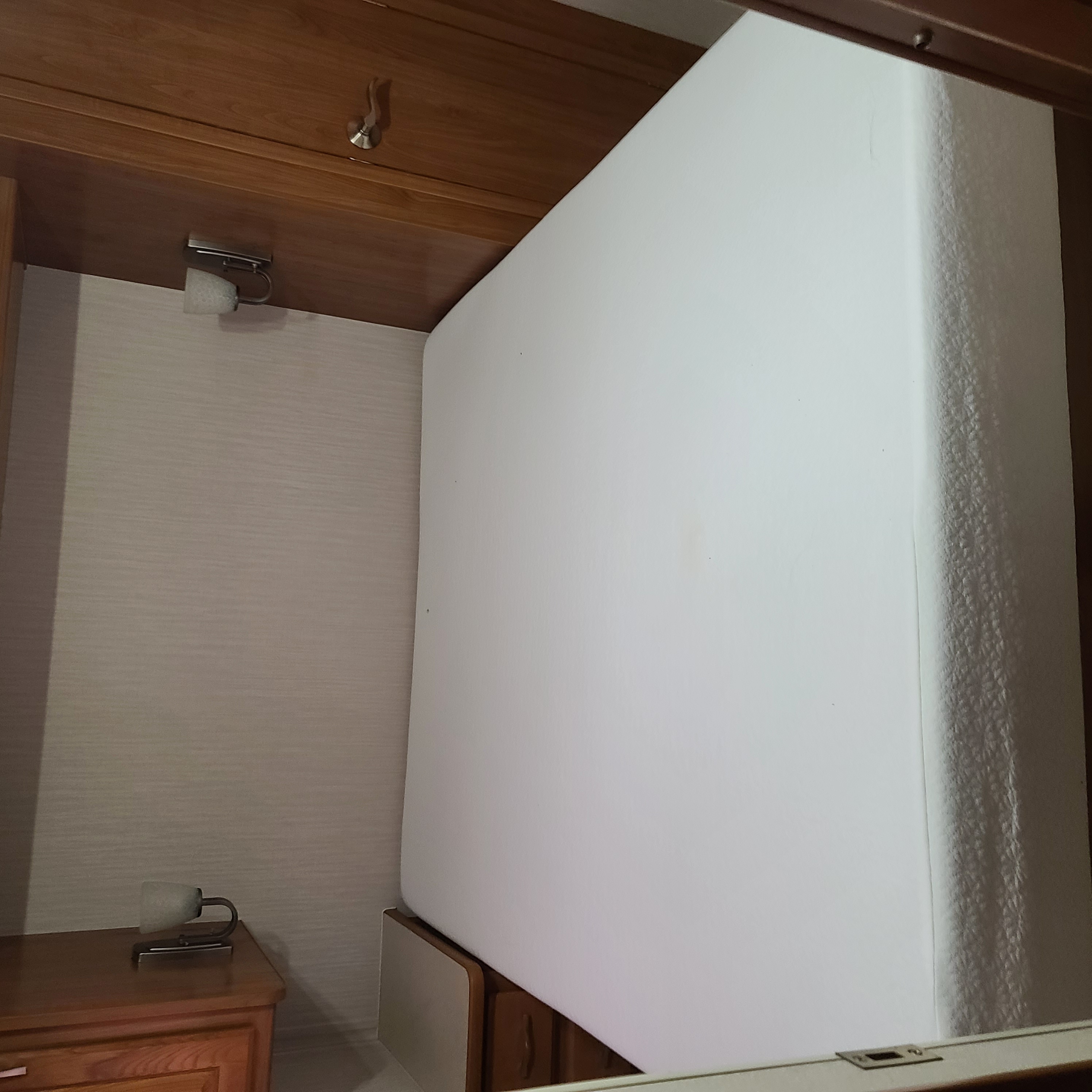 RV rental bedroom: a white mattress is positioned vertically, surrounded by wooden cabinetry, reading lights, and a nightstand.. Coachmen Aurora 2001