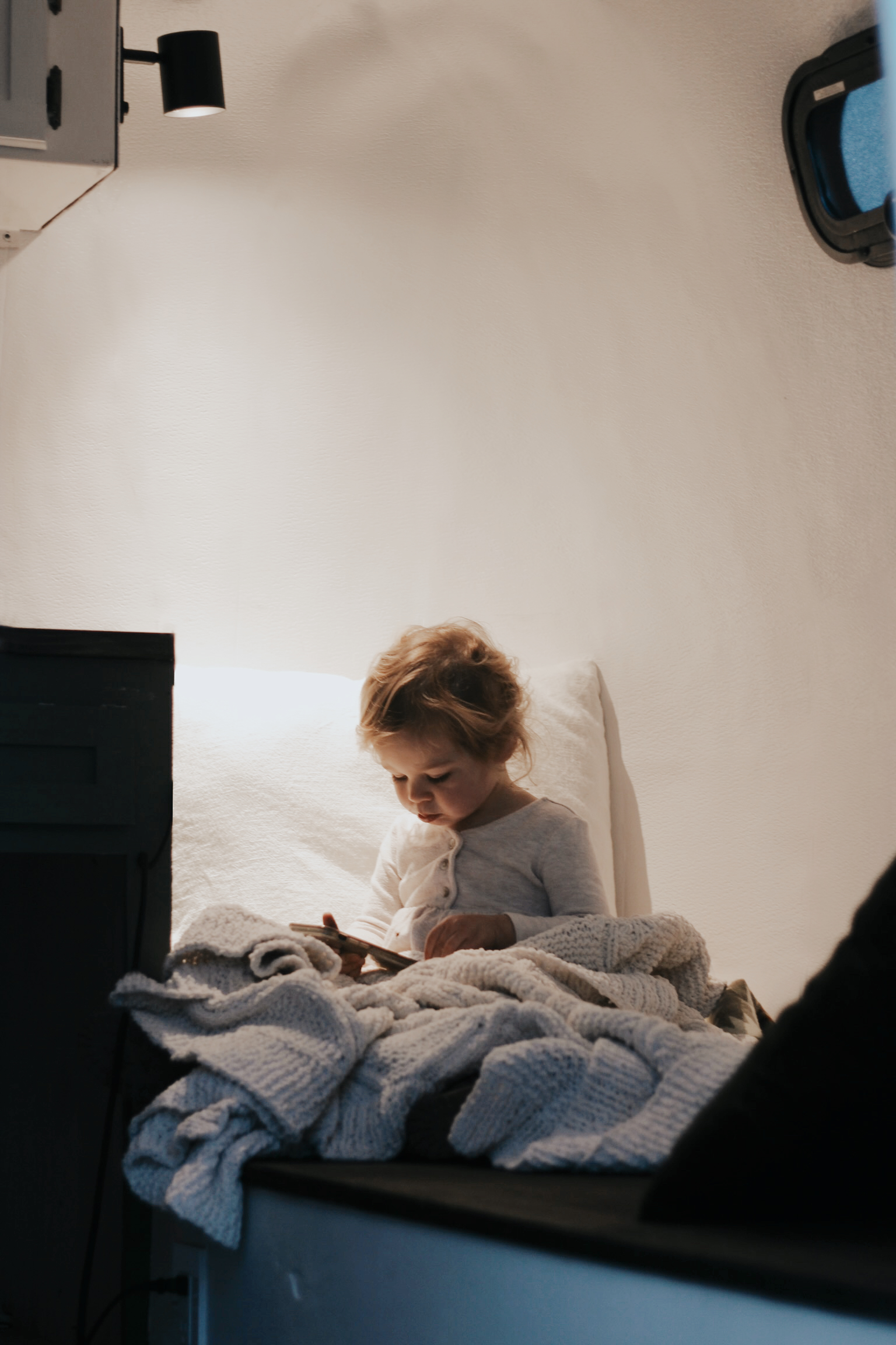 Cozy rv rental interior: A young child, bundled in a blanket, looks at a device, illuminated by a warm lamp.. Scamp Scamp Trailer 2005