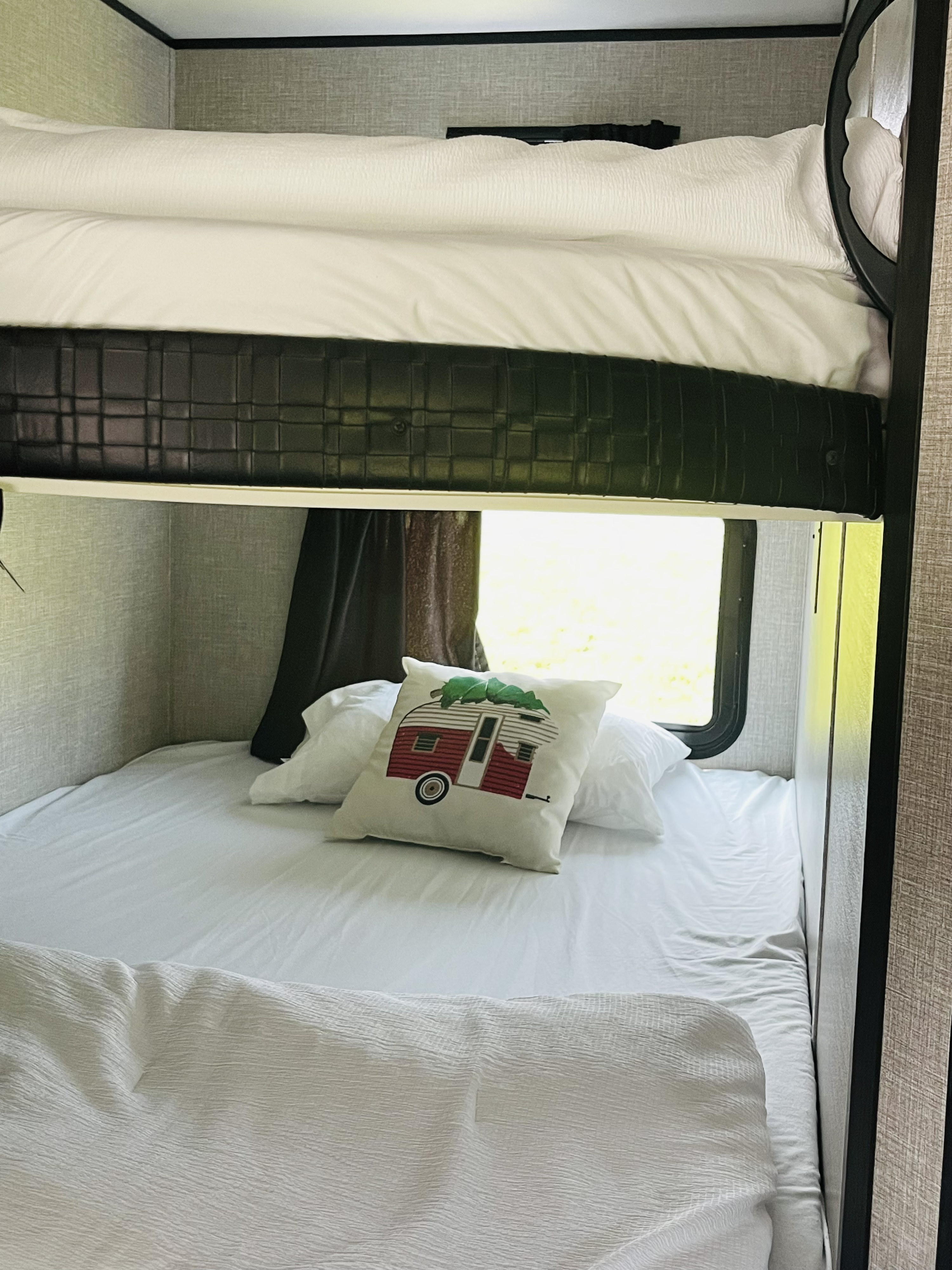 An RV rental's interior shows cozy bunk beds with white bedding & a decorative camper pillow by a bright window.. Jayco Jayco Flight 2019