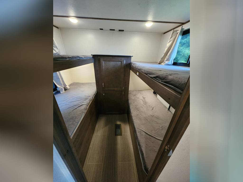 Spacious RV rental bunkhouse featuring four cozy beds and central storage, ideal for family adventures.. Keystone RV Passport SL 2021