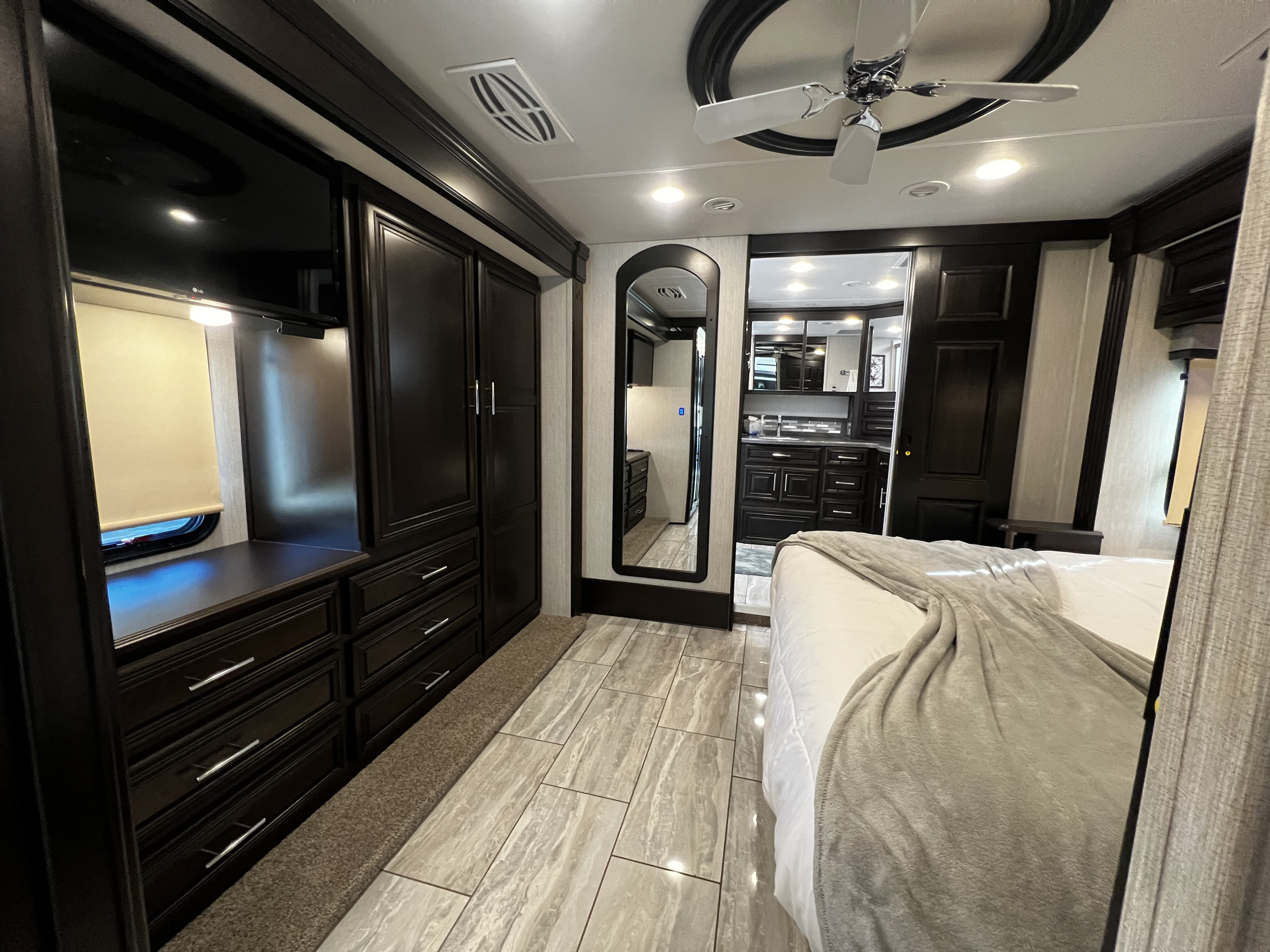 Spacious RV rental bedroom with dark wood cabinetry, TV, and elegant tiled floors, leading to a functional living area.. Forest River Berkshire 2022