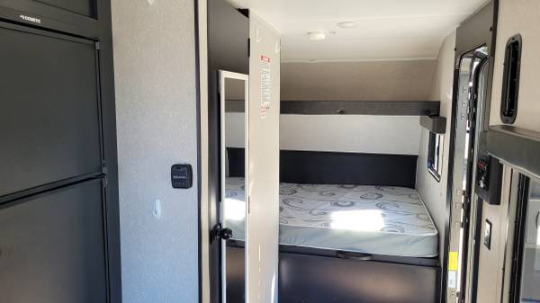 View of a compact RV rental interior, showing a fridge, control panel, and a cozy bedroom with a patterned mattress.. Forest River Cherokee Wolf Pup 2021
