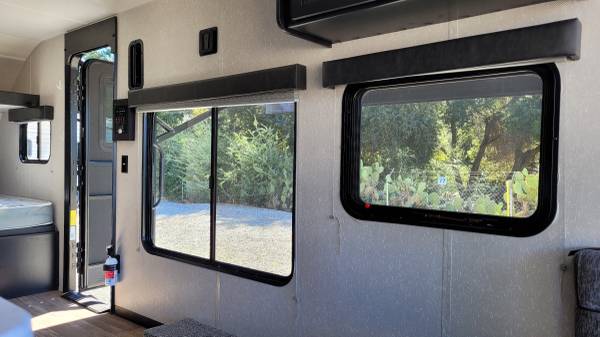 Bright rv rental interior: large windows revealing trees/cacti, open door, and bed. Your journey awaits!. Forest River Cherokee Wolf Pup 2021