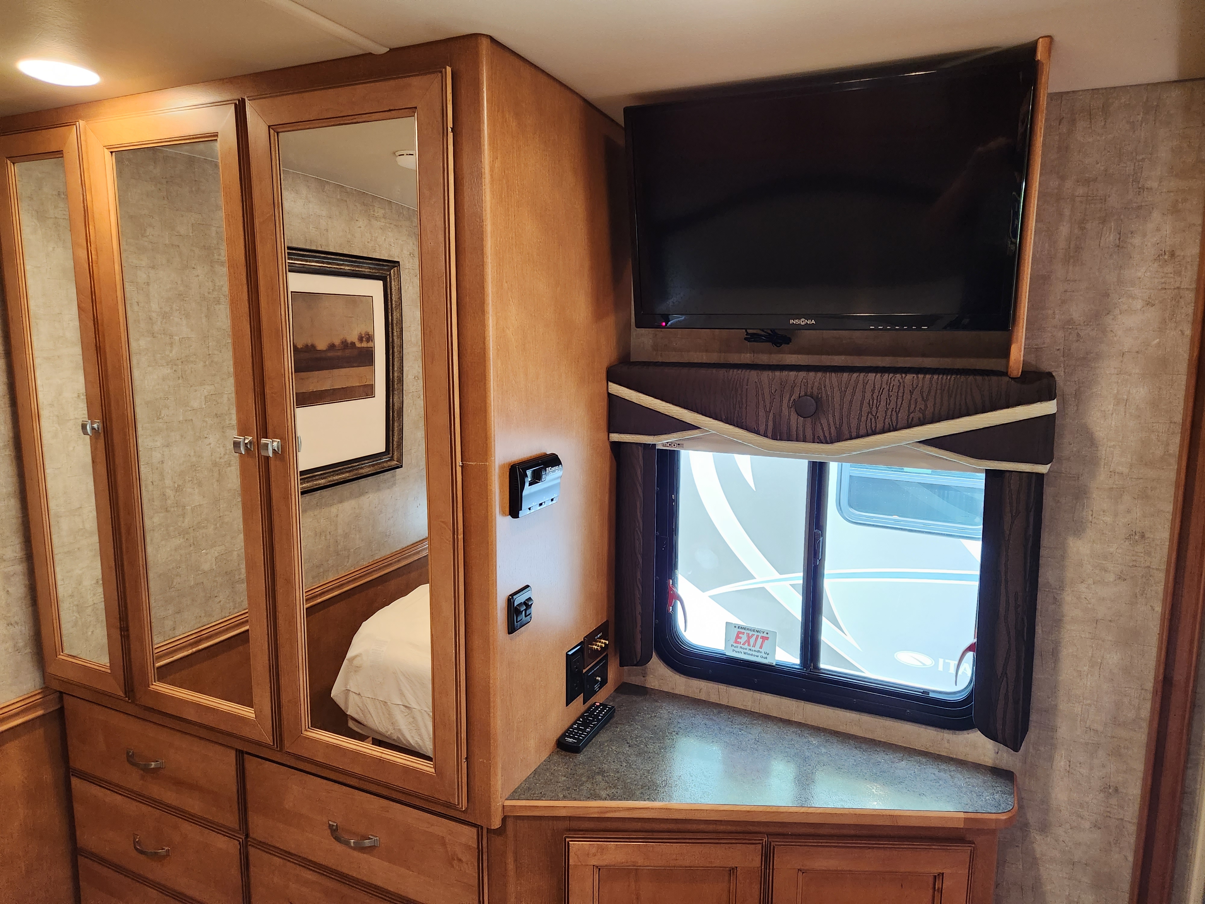 Cozy RV rental bedroom area featuring a mirrored wardrobe, TV, and emergency exit window. Ample storage included.. Itasca Sunova 2015