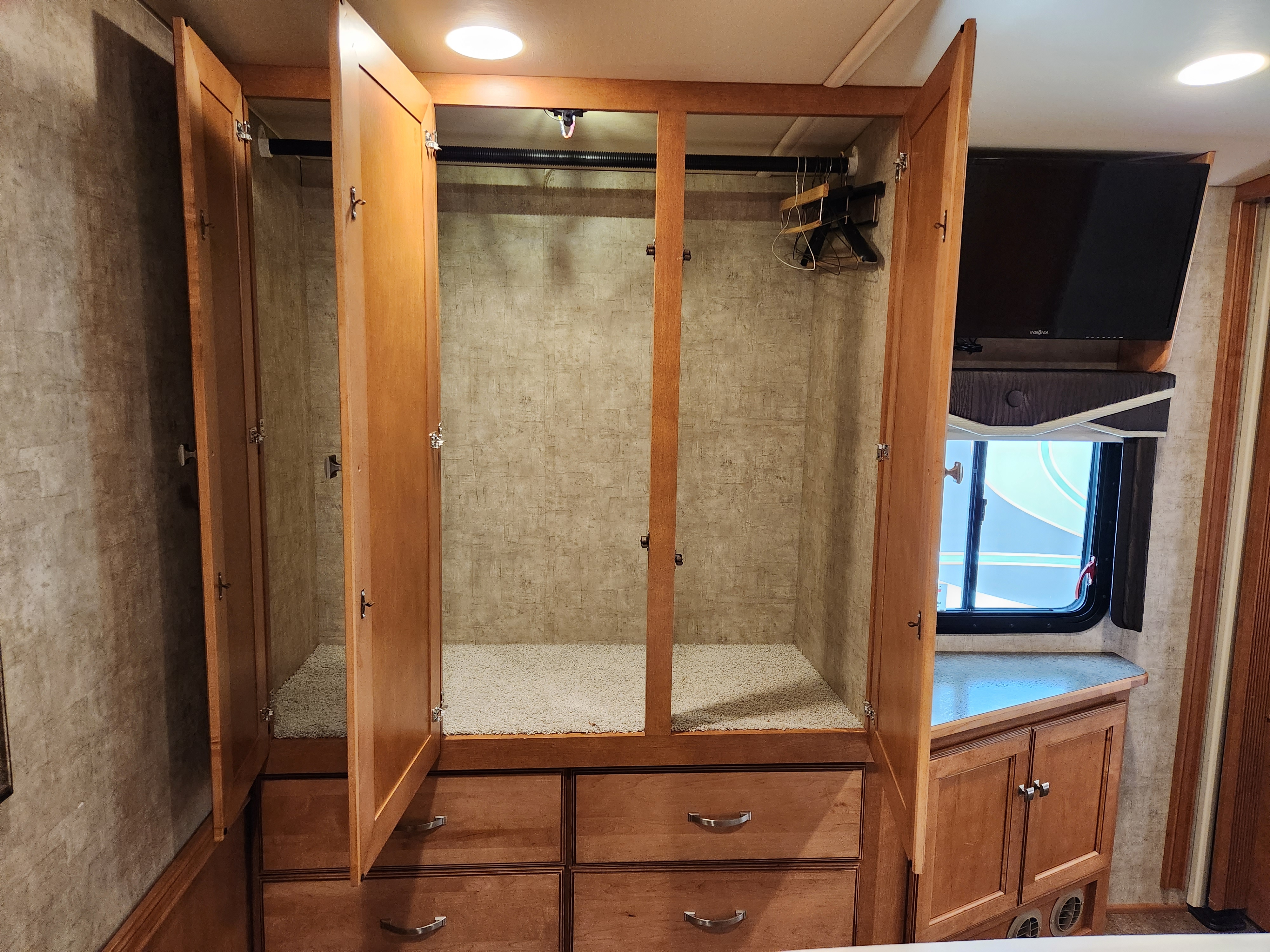 Spacious RV rental closet with open doors, hangers, and drawers, next to a TV and window. Ideal for comfortable travel.. Itasca Sunova 2015