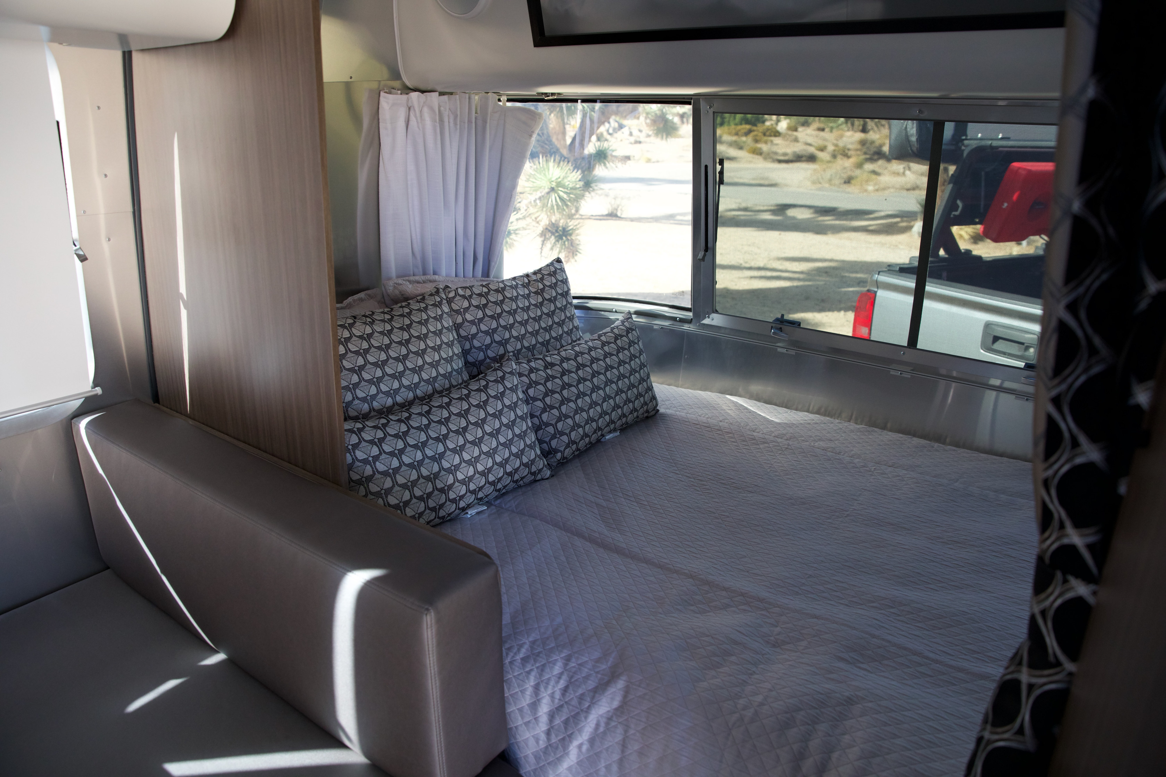 Cozy RV rental interior with a comfy bed, large windows showing a desert view and truck. Perfect for travel adventures.. Airstream Caravel 2022