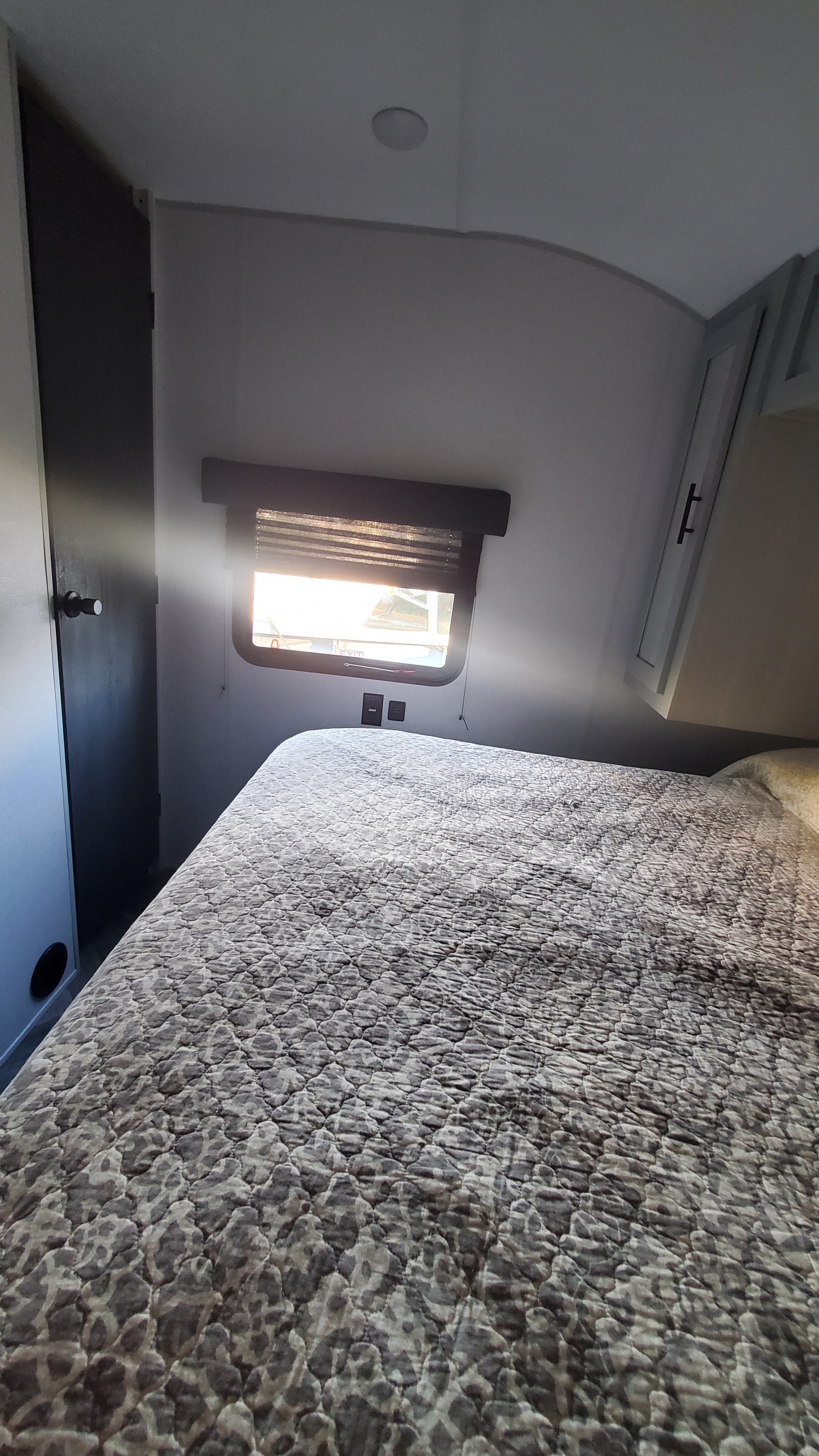 Cozy RV rental bedroom featuring a bed with patterned comforter, window, and overhead storage for your trip.. Forest River Wildwood 2022