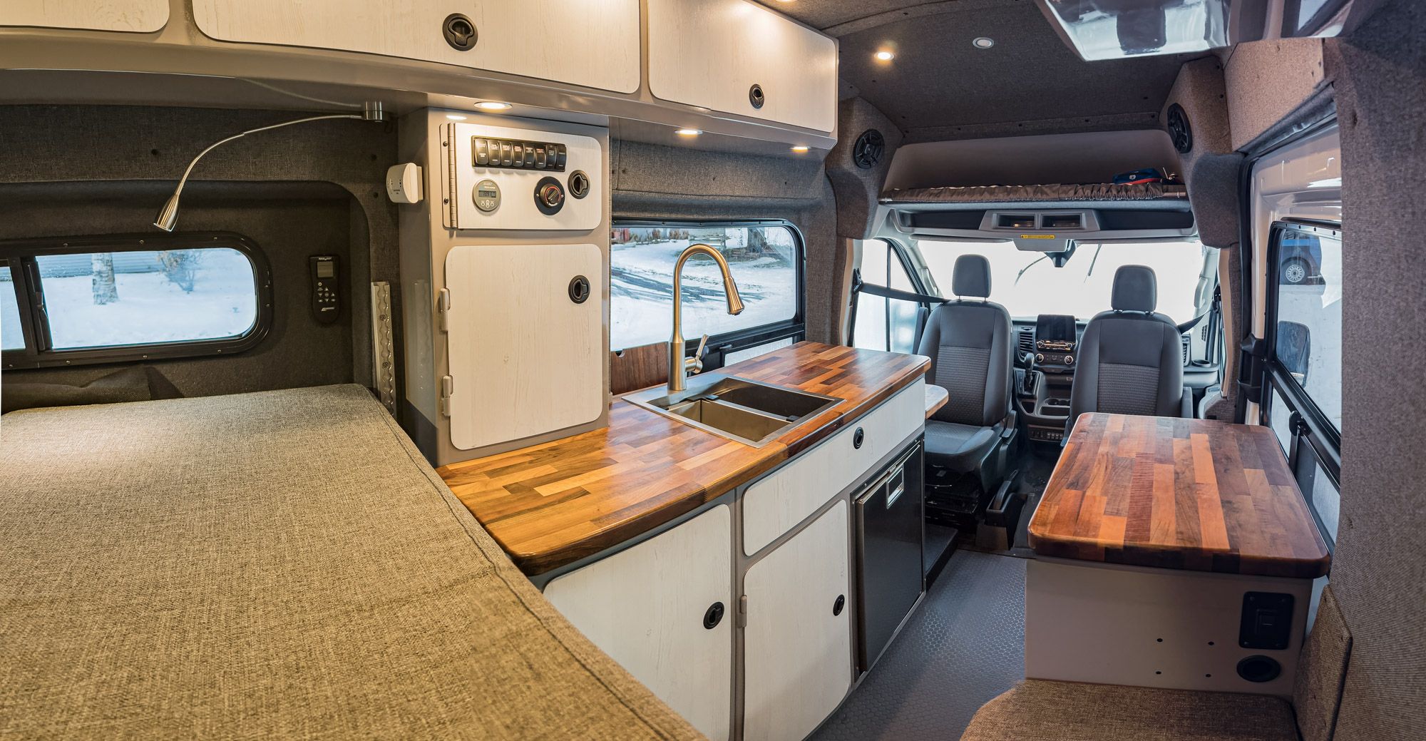 Cozy RV rental interior featuring a full bed, modern kitchenette, and convertible living space for comfortable travels.. Ford Transit 2020