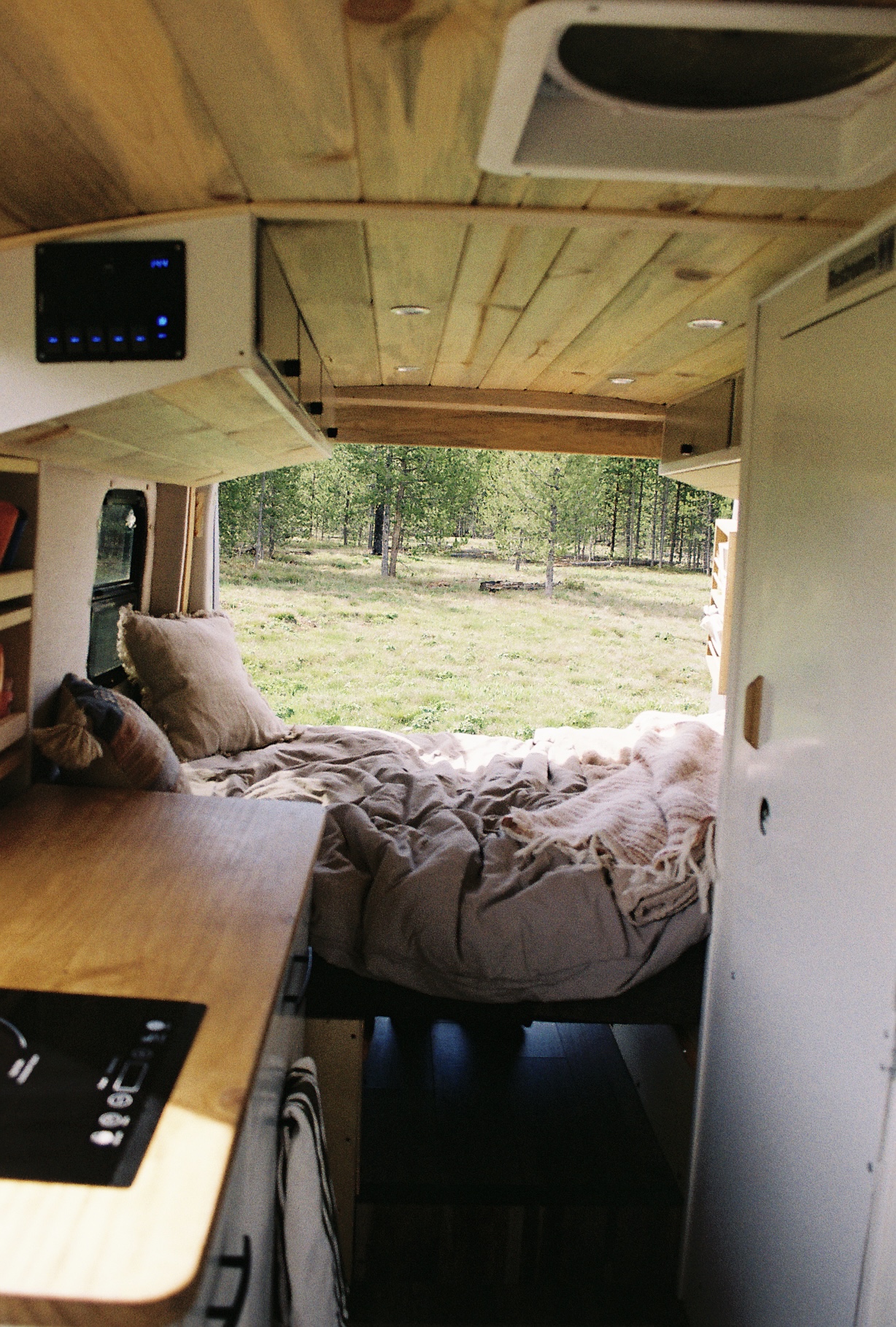 Experience van life: a cozy RV rental interior with a bed facing a lush green forest, ideal for outdoor travel.. Ford Transit 2016