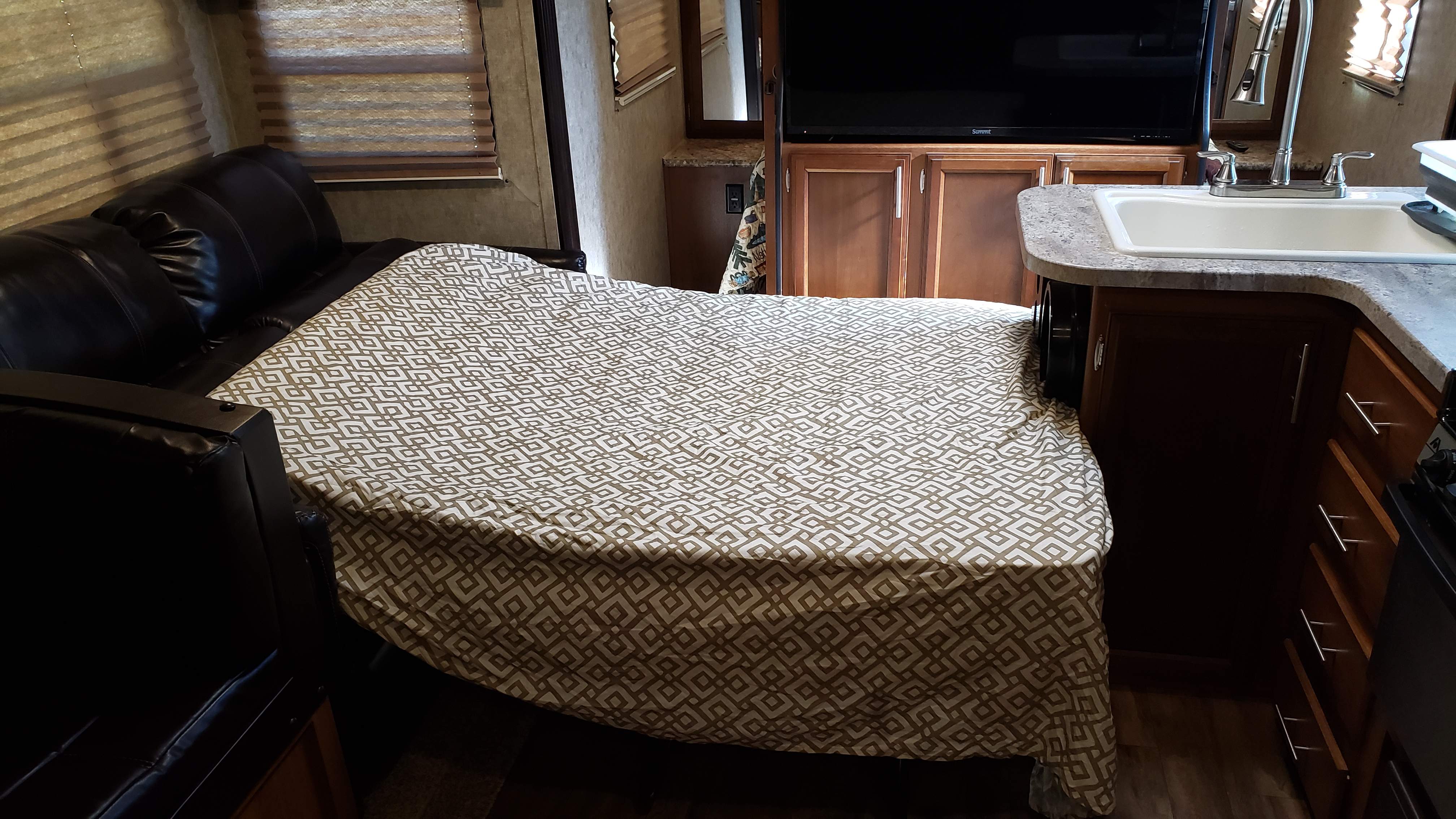 Inside an RV rental: a patterned sofa-bed fills the living area, with a kitchen sink & TV visible.. Prime Time Tracer Air 285 2018