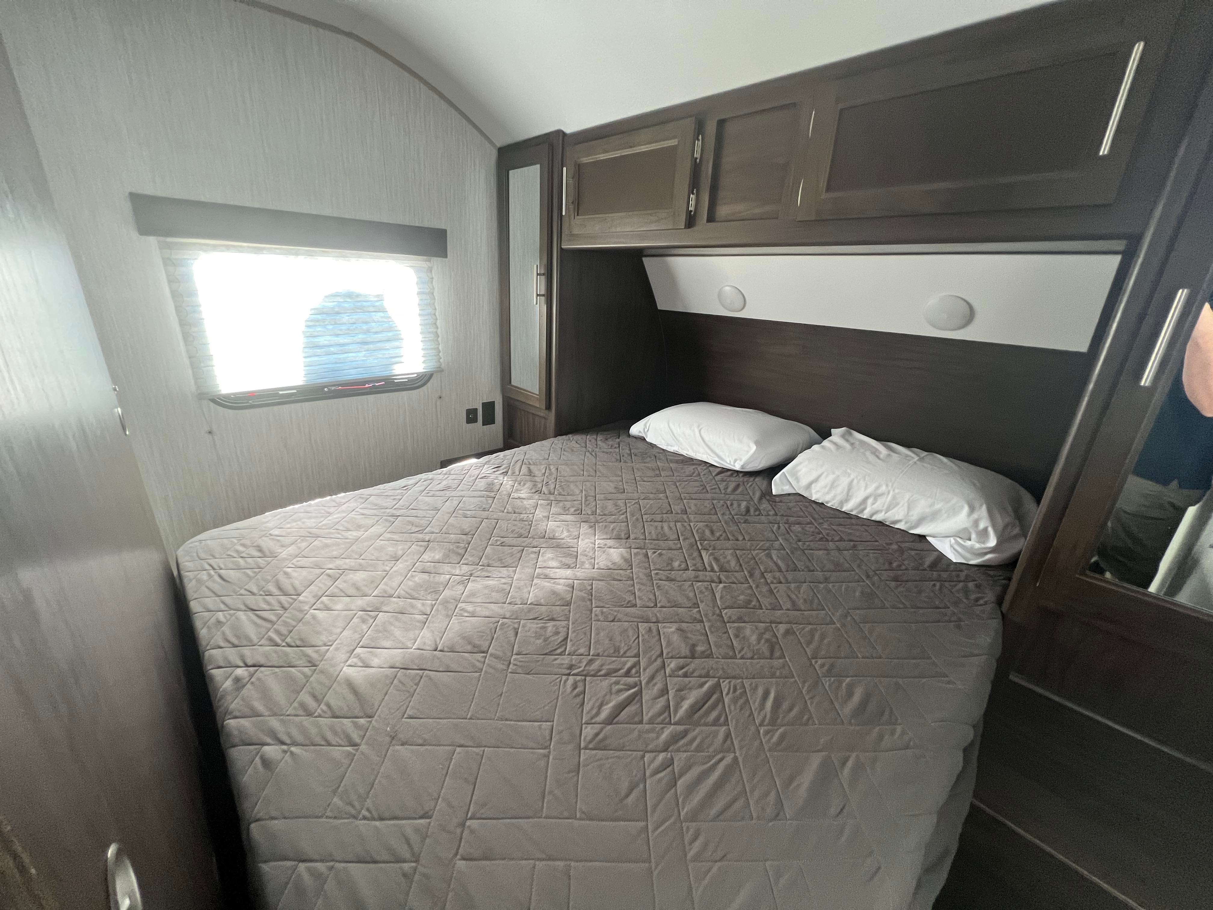 Cozy RV rental bedroom with a comfy bed, overhead cabinets, and a bright window. Ideal for your next adventure.. Forest River Cherokee Grey Wolf 2020