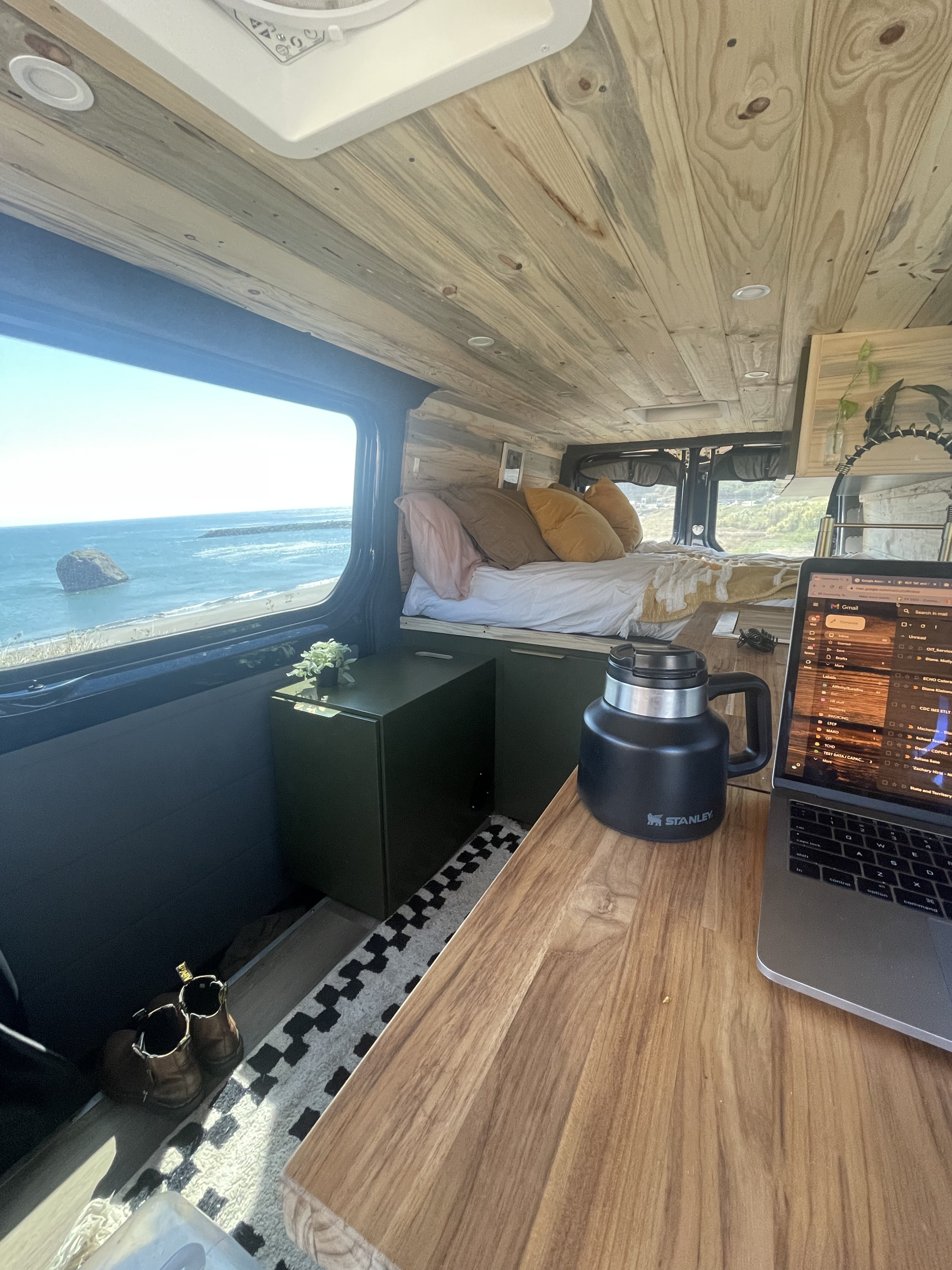 RV rental with a view! Cozy camper van interior featuring a comfortable bed and a mobile office with a laptop overlooking the ocean.. Mercedes-Benz Sprinter 2016