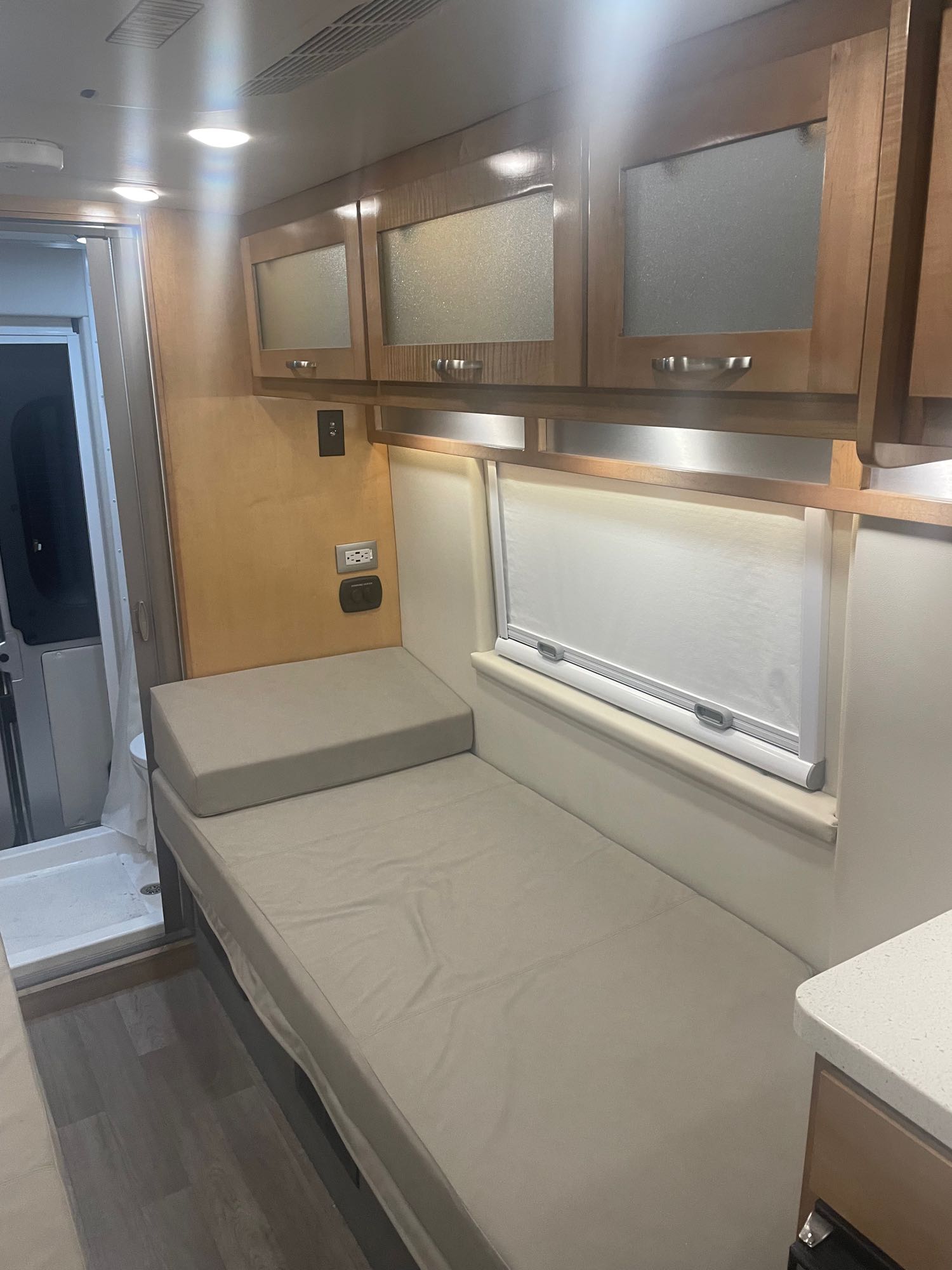 RV rental interior: light wood cabinets, comfortable bench seating (converts to bed), window, and compact shower visible.. Coachmen Nova 2021